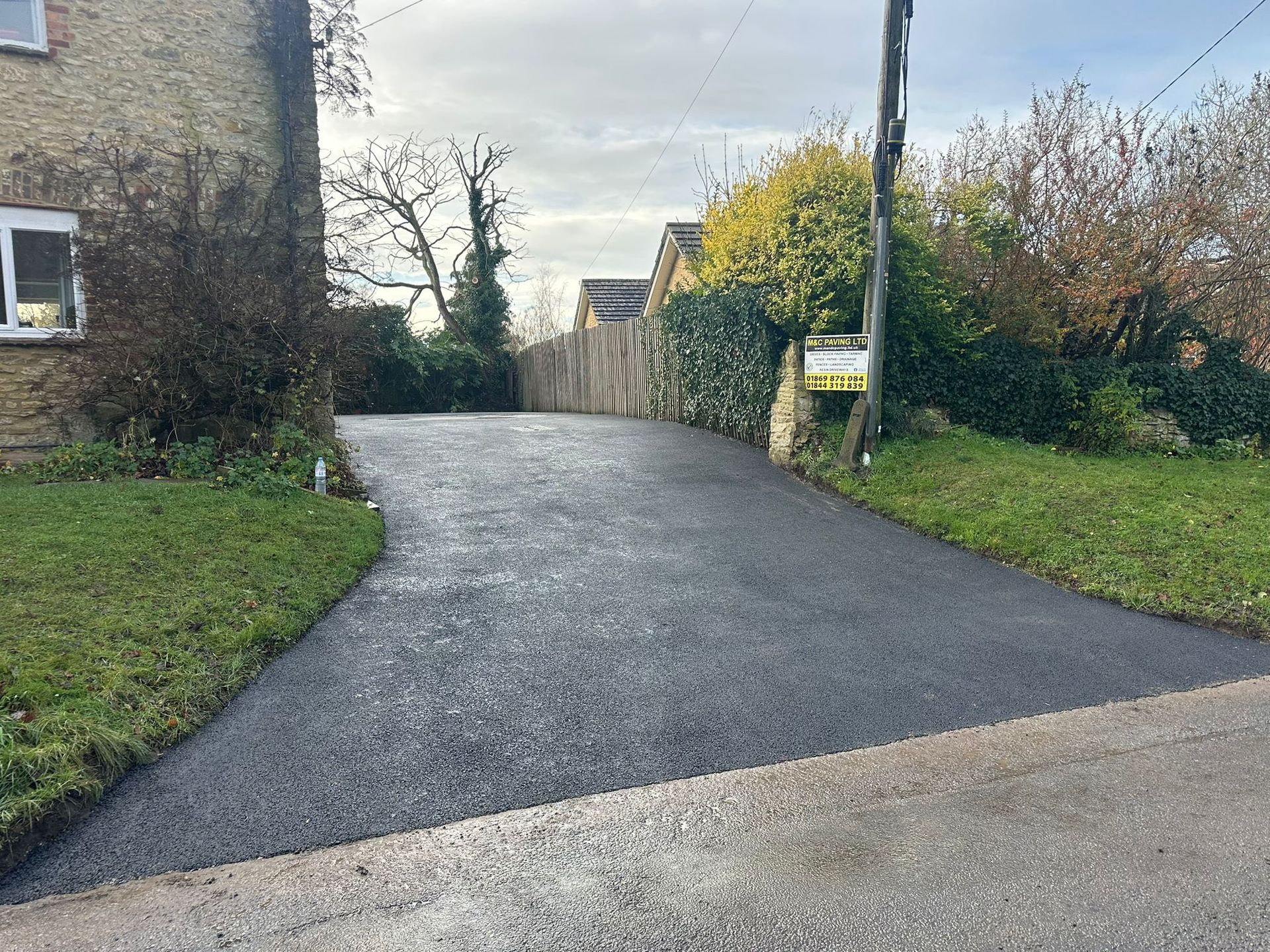 A paved driveway curves uphill between grassy banks and stone walls on an overcast day.
