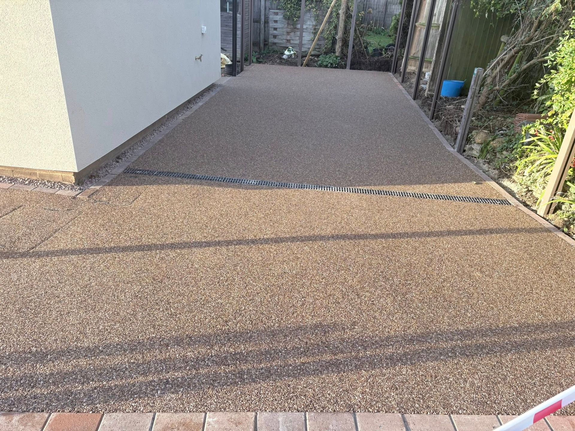 Gravel driveway beside a white wall, with sunlight and shadows across the path.