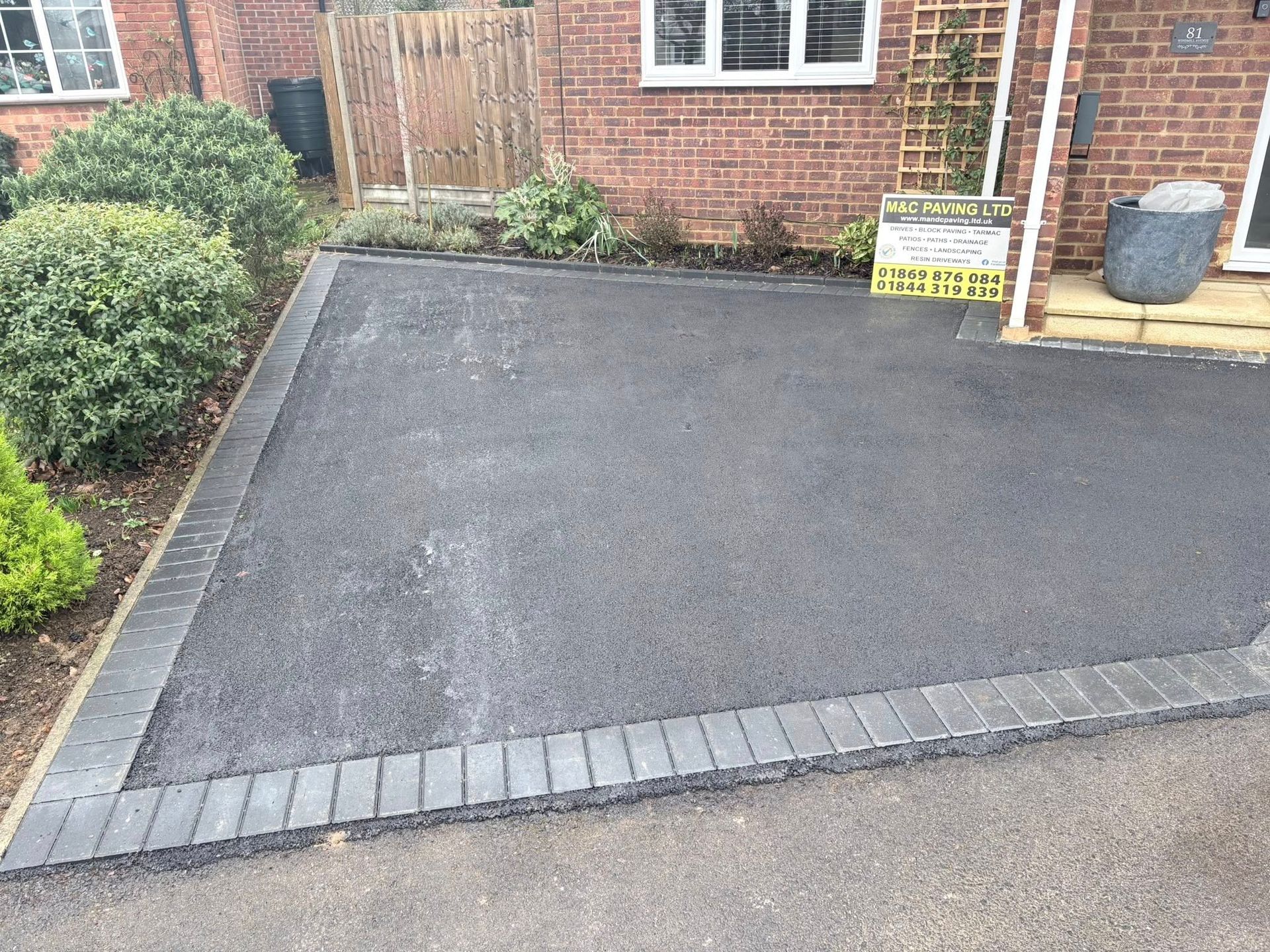 Freshly paved black driveway in front of a brick house, with a small sign near the entrance