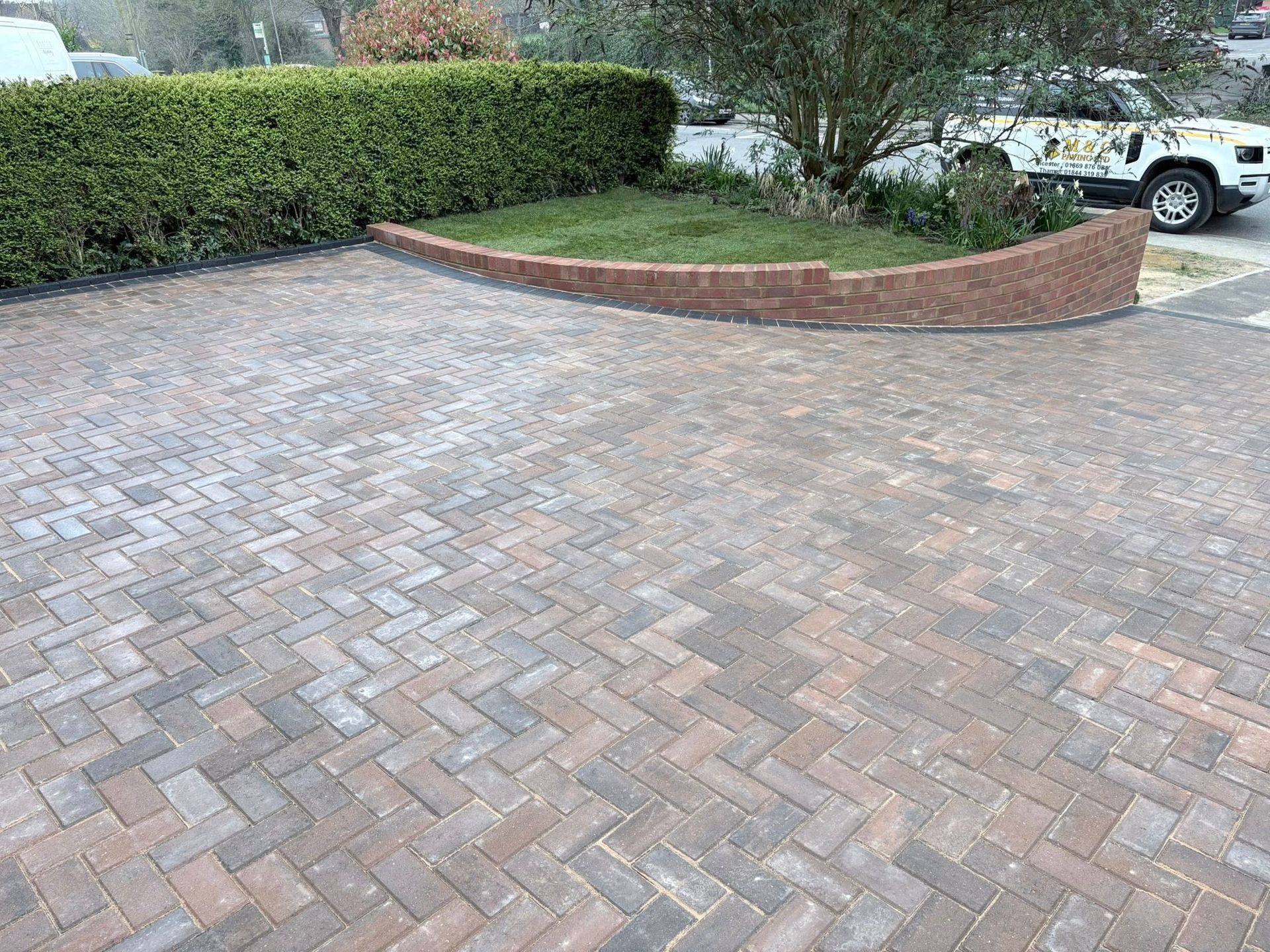Brick driveway with a curved brick planter and hedges, with a white car parked at the top right.