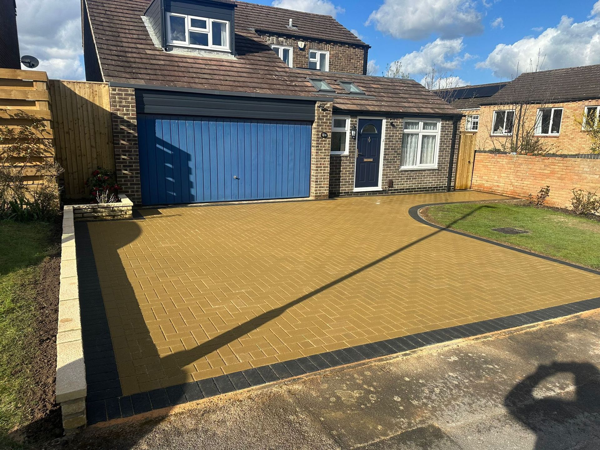 Backyard patio with blue garage doors and a paved driveway in front of a house.