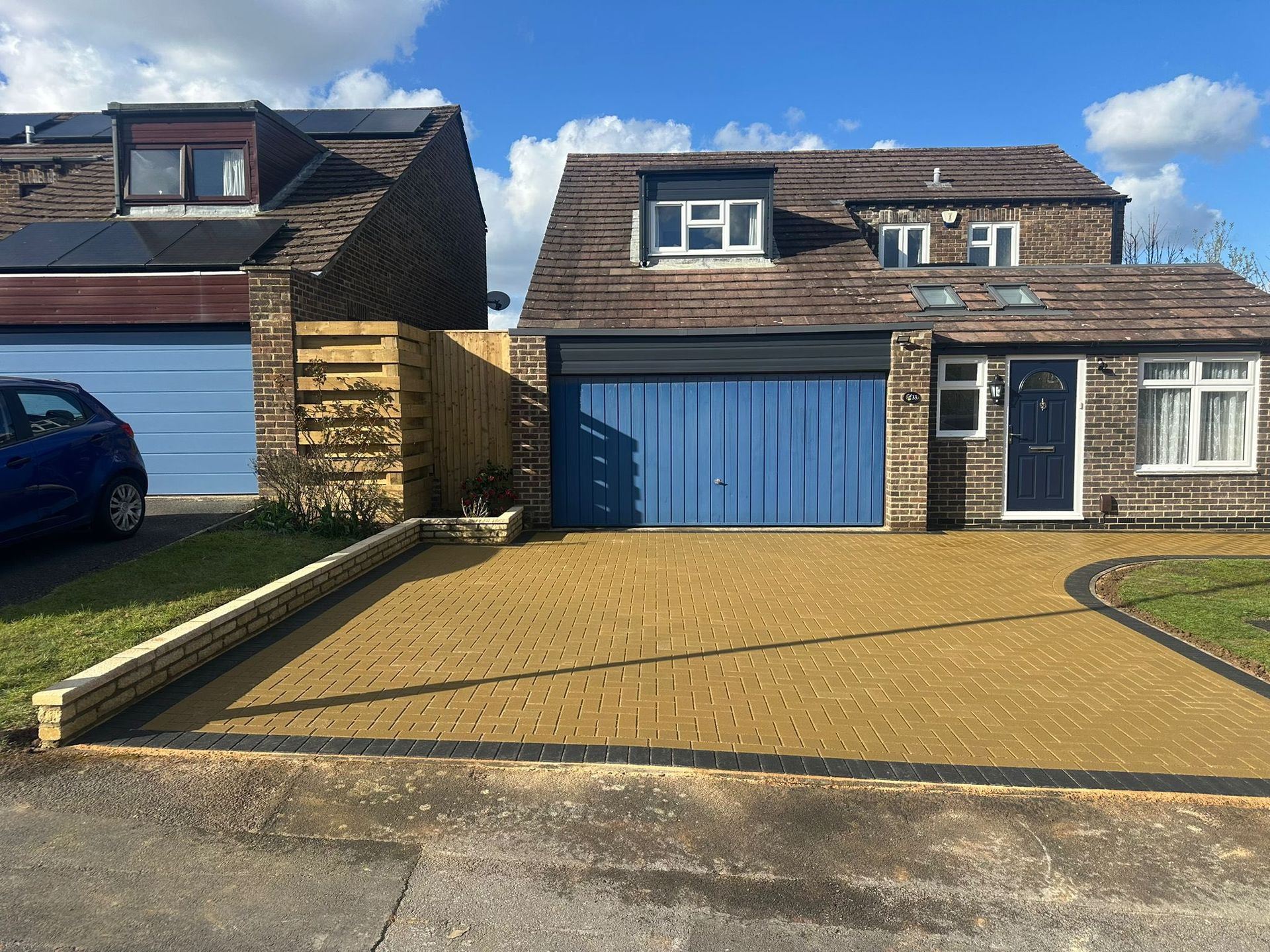 Blue garage doors and a stone house with a tan driveway in a residential neighborhood