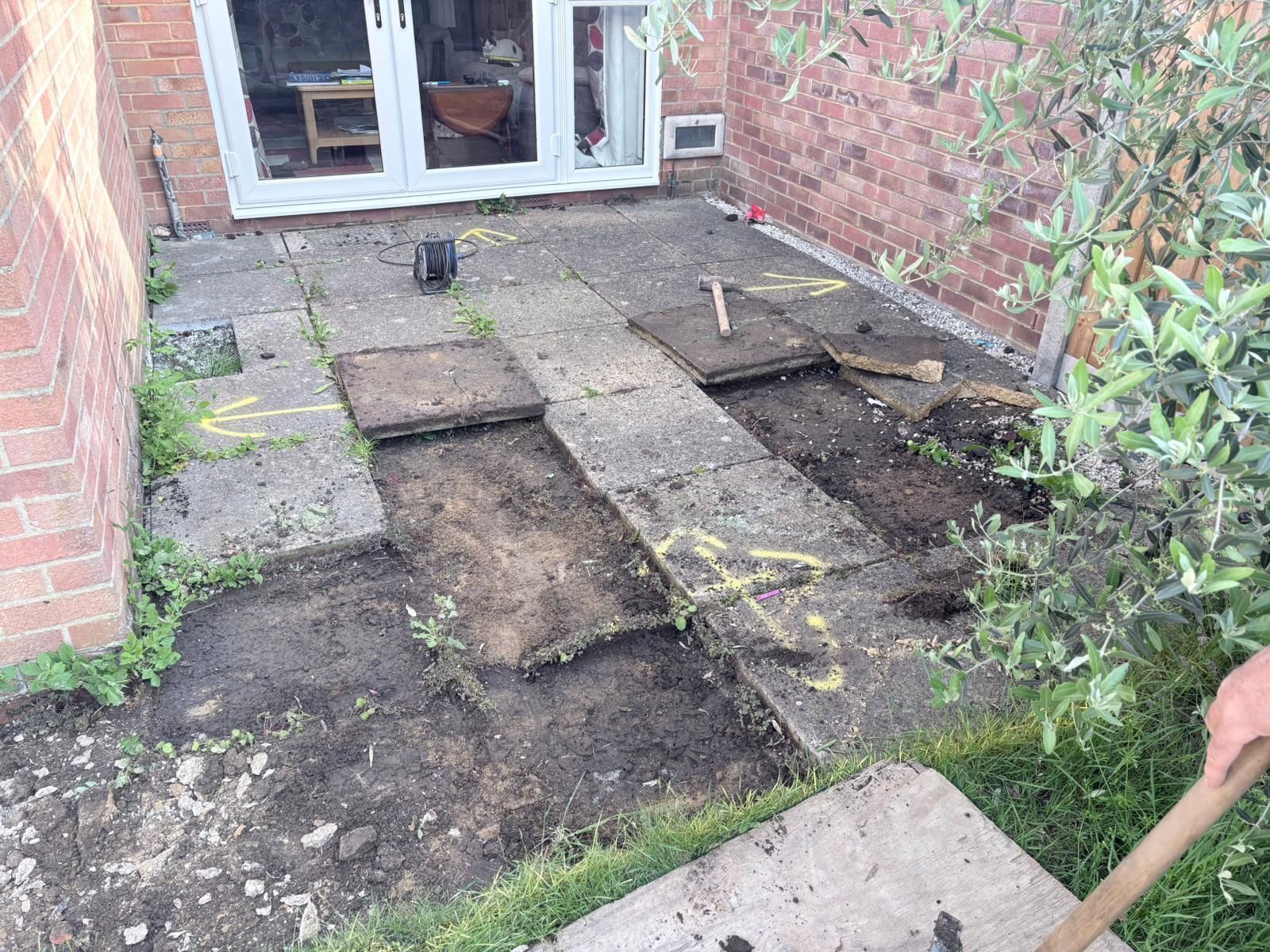 Stone patio and garden path leading to a house with glass doors, bordered by flowers and greenery.