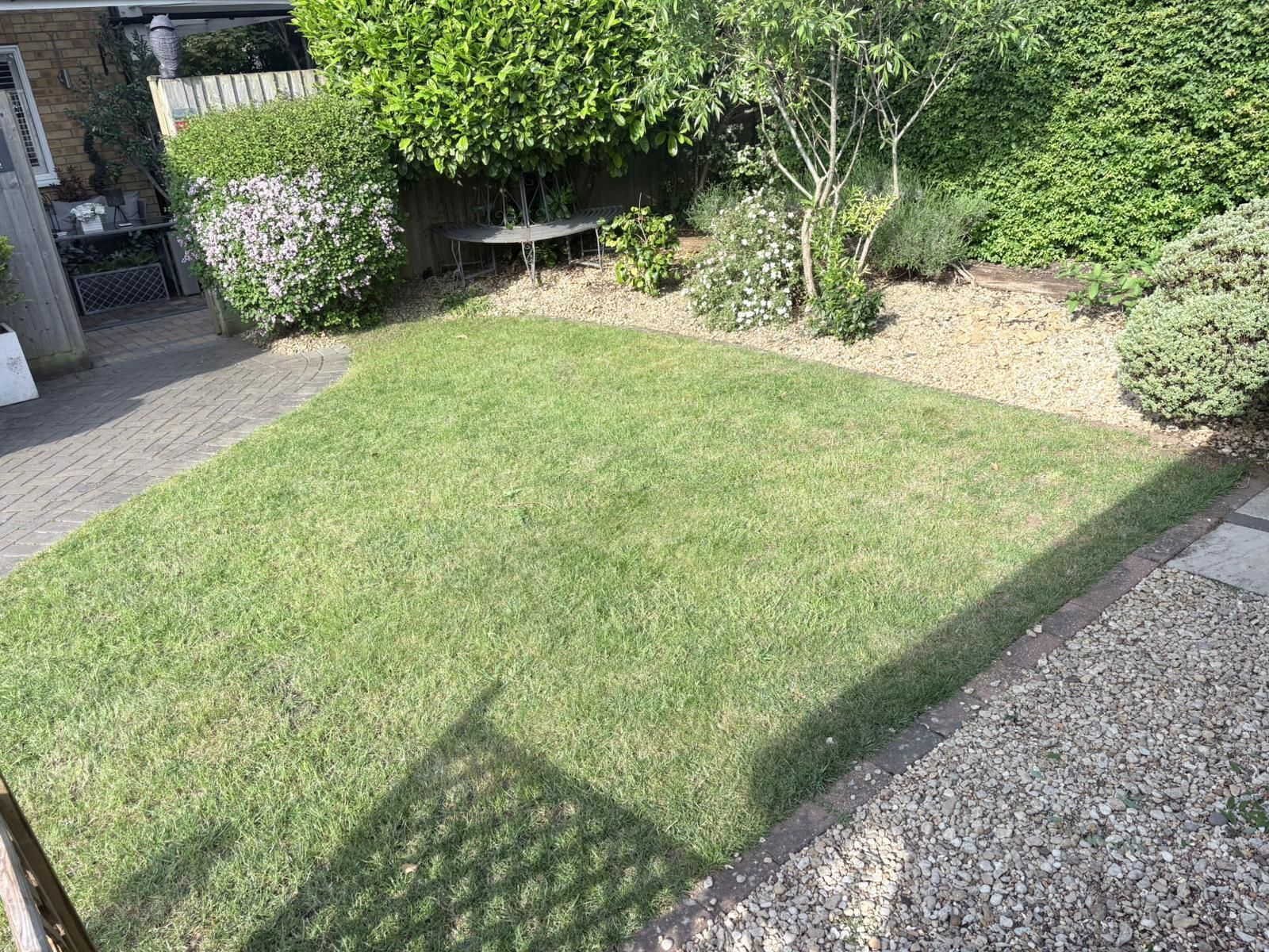 Residential driveway with wooden fence, gravel edges, and a garage in the background.