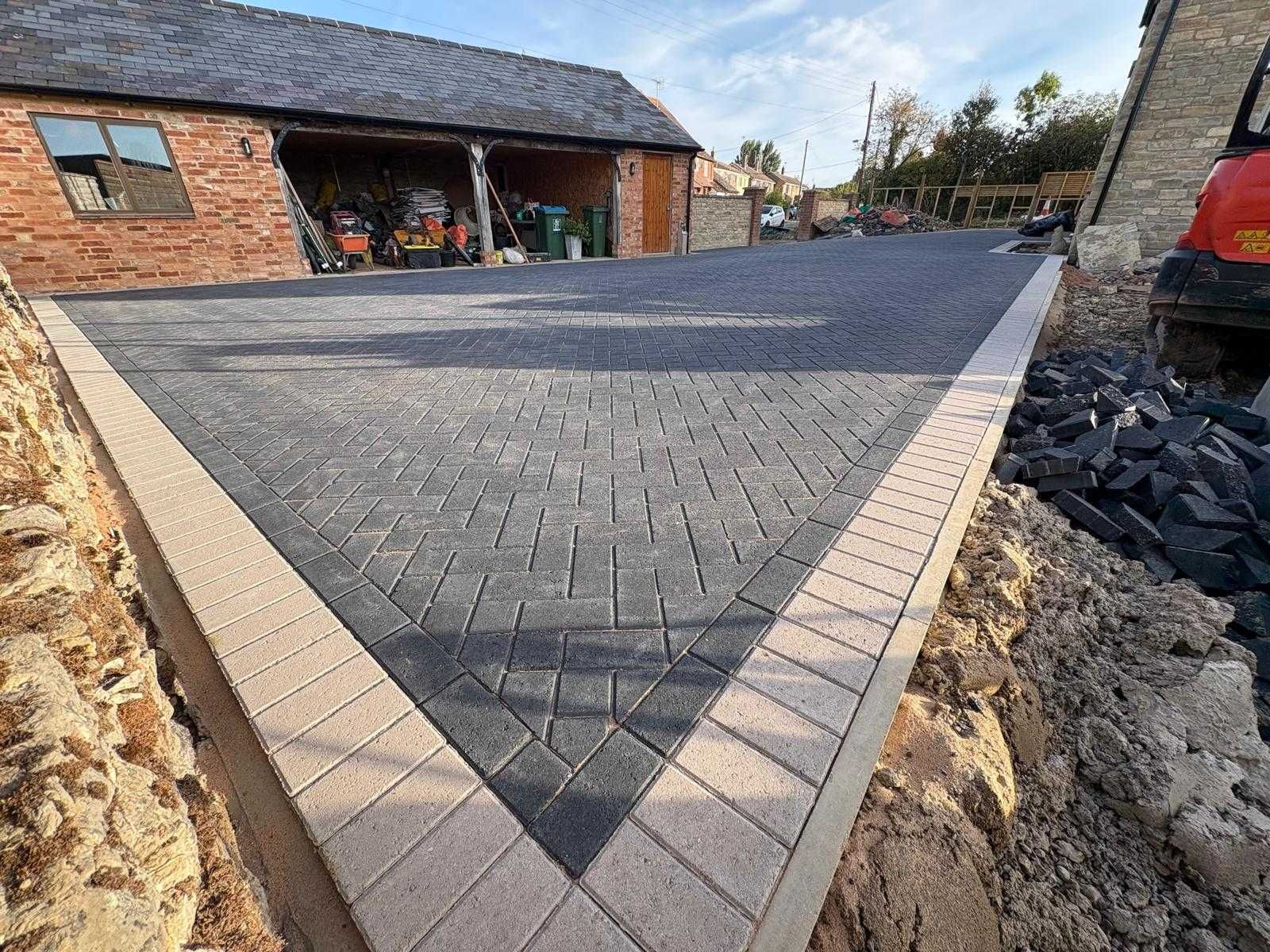 Triangular paved driveway area with gray pavers beside a brick house under construction
