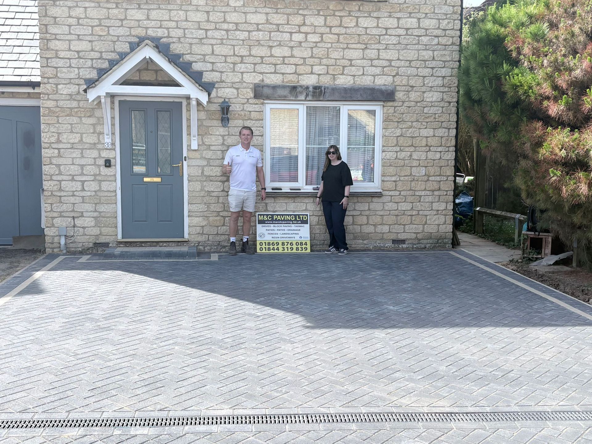 Freshly paved driveway beside wooden fences and houses, with an M&C Paving Ltd sign in the foreground
