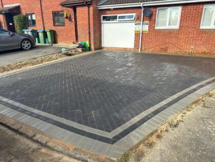 Brick-paved driveway with dark gray paving and light gray border in front of a house and garage.