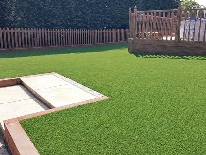 Backyard with bright green artificial turf, stone patio, and a wooden deck fence in the background