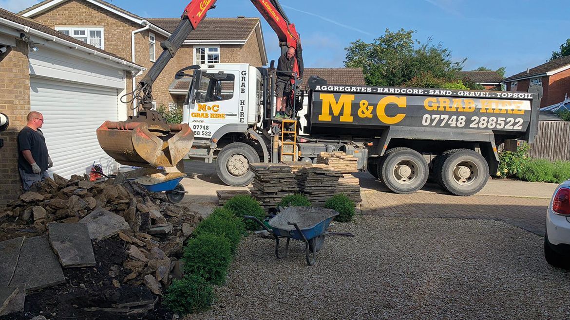 Skip loader and dump truck removing rubble in a residential driveway on a sunny day