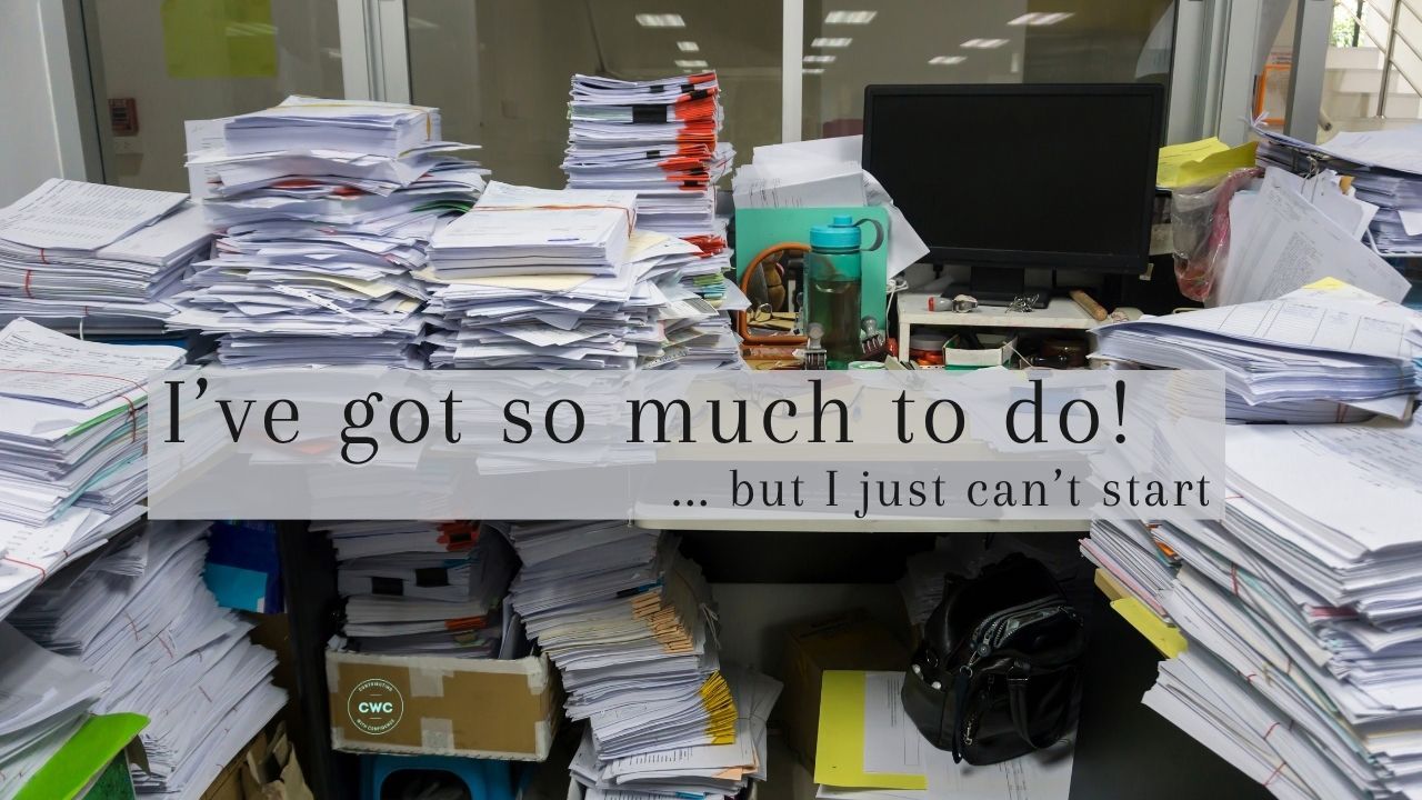 A very messy desk with piles of paper with wording I've got so much to do... but I just can't start