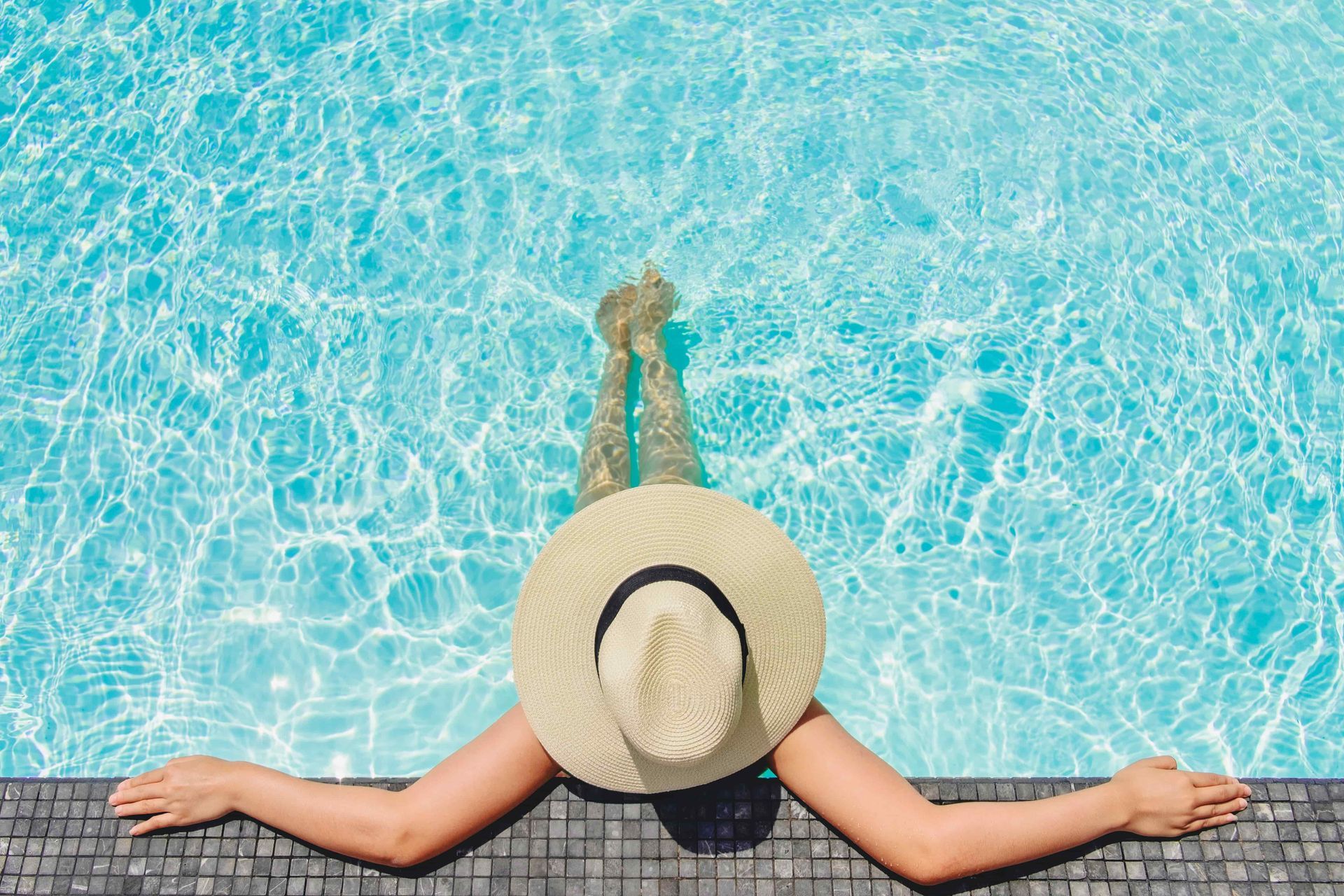Woman relaxing in pool, wearing a hat, arms resting on the edge.