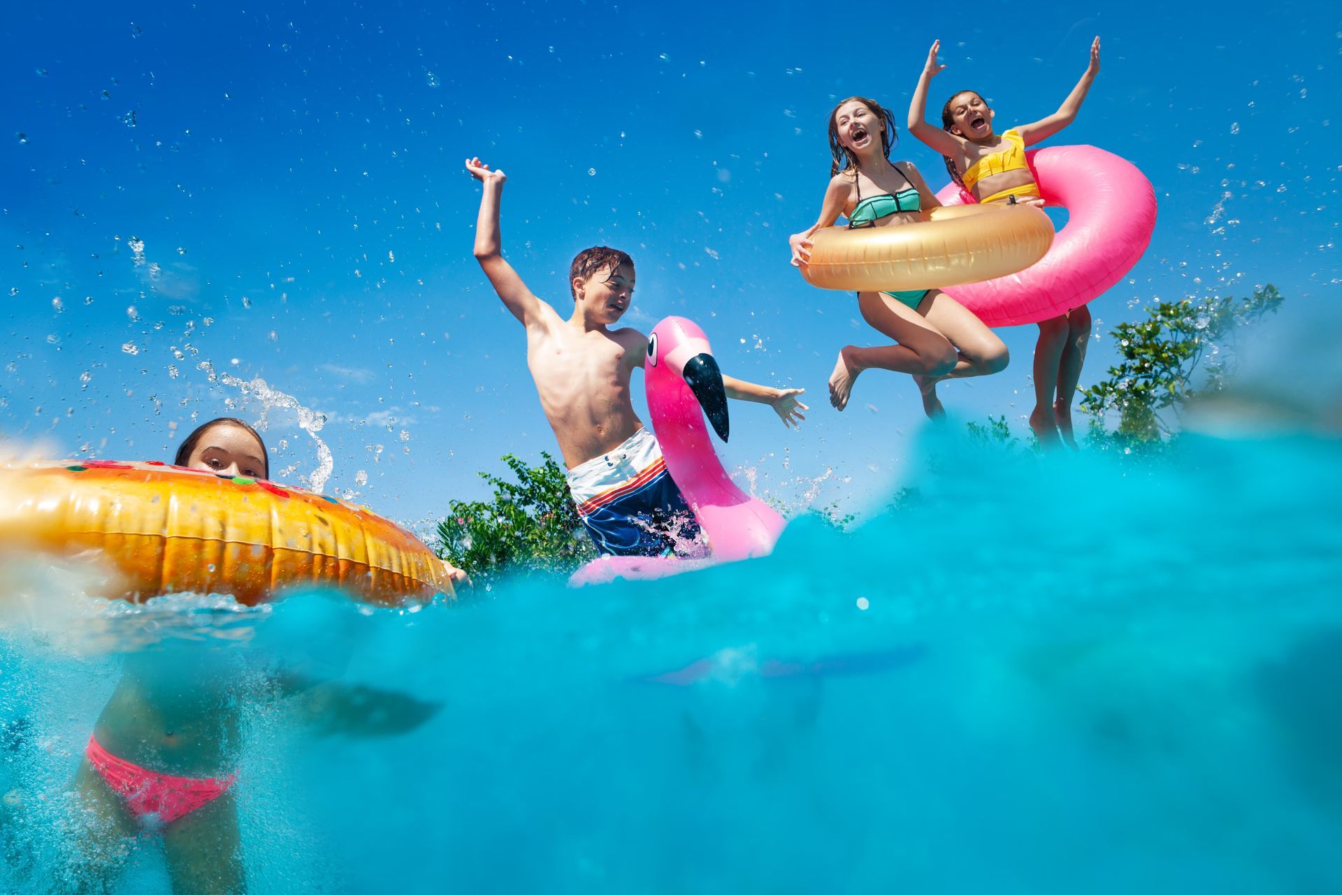 People jumping into a pool with inflatables on a sunny day.