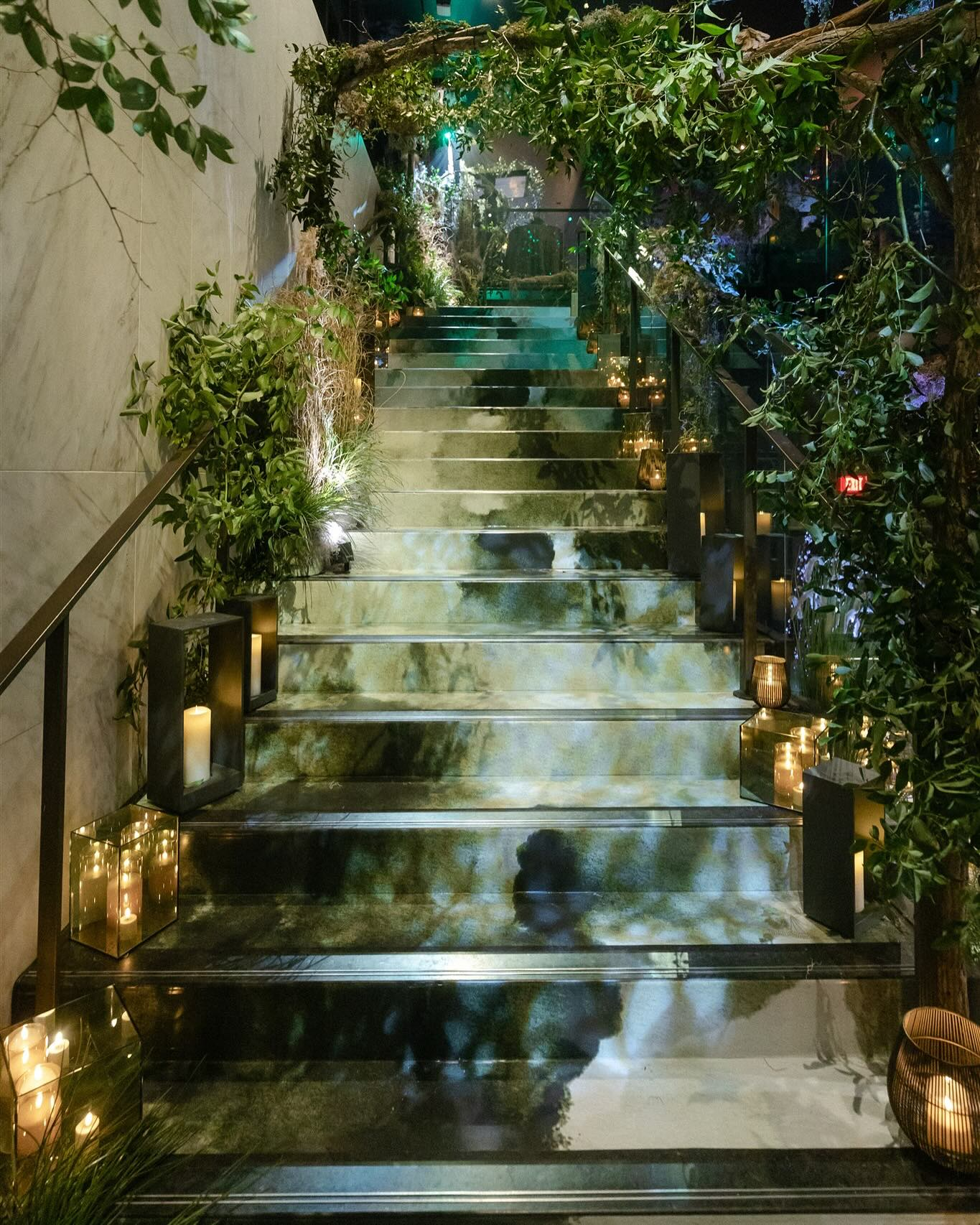 Illuminated stone staircase lined with candles and greenery at night