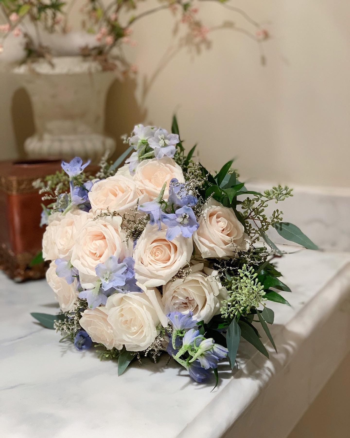 White and pale pink rose bouquet with blue accents on a table indoors