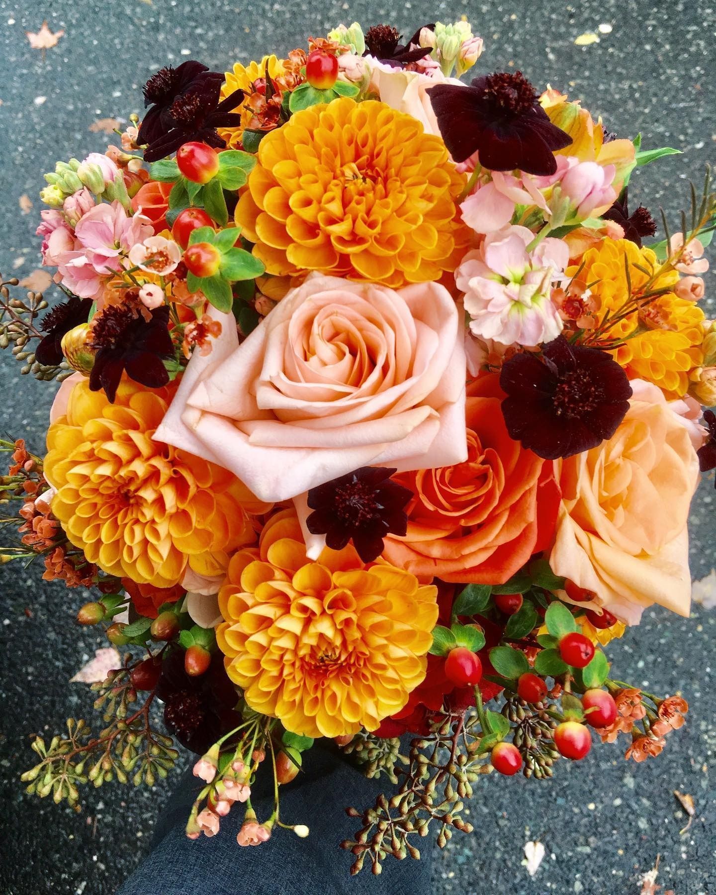Colorful floral bouquet with peach, pink, yellow, and burgundy flowers on a dark background