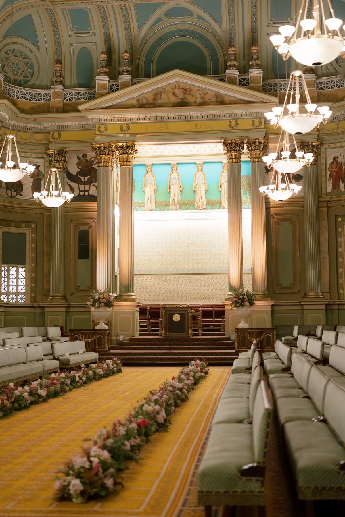 Elegant ornate banquet hall with chandeliers, gold decor, and long rows of white chairs facing a stage