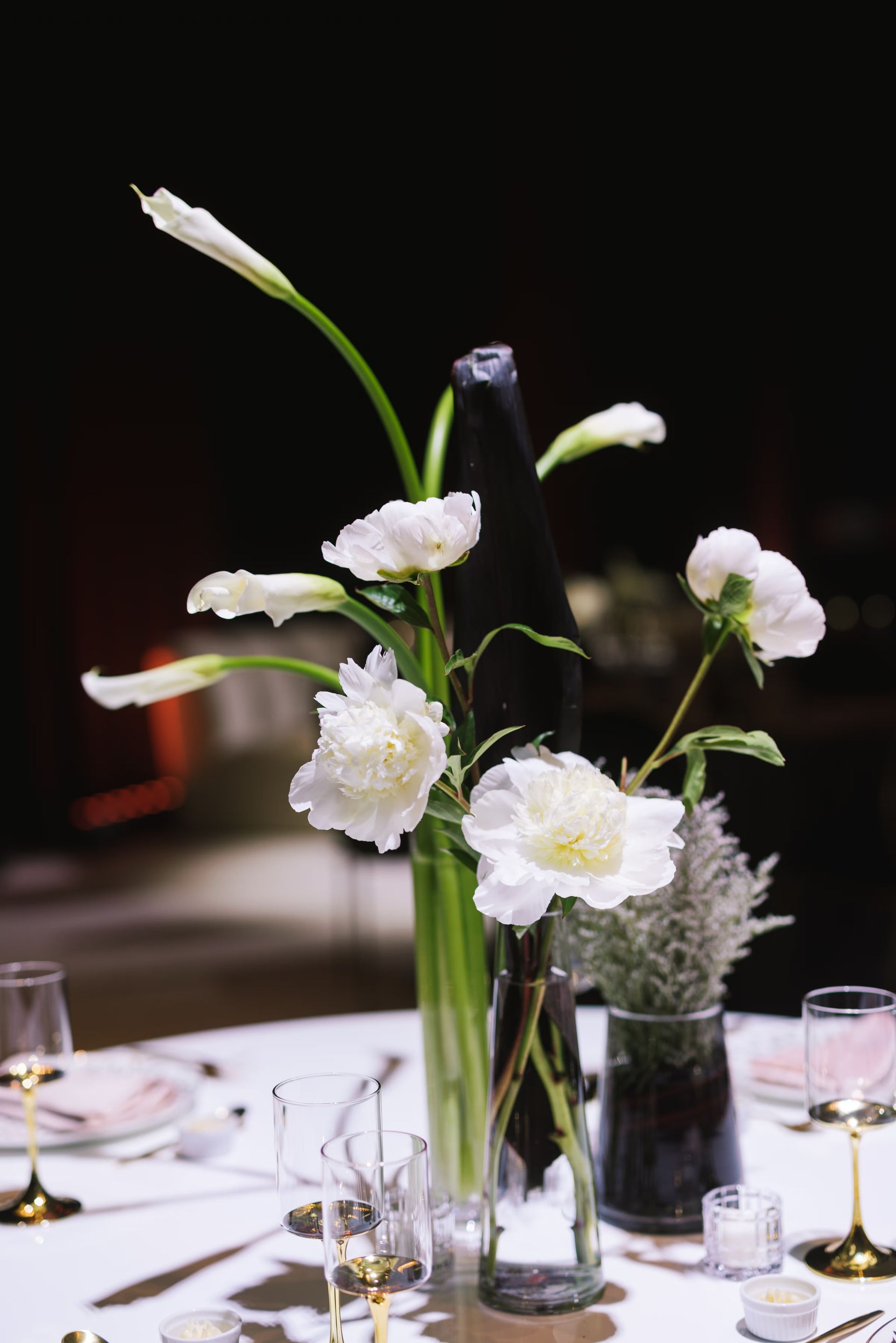 White flowers in a tall glass vase centerpiece on a candlelit table