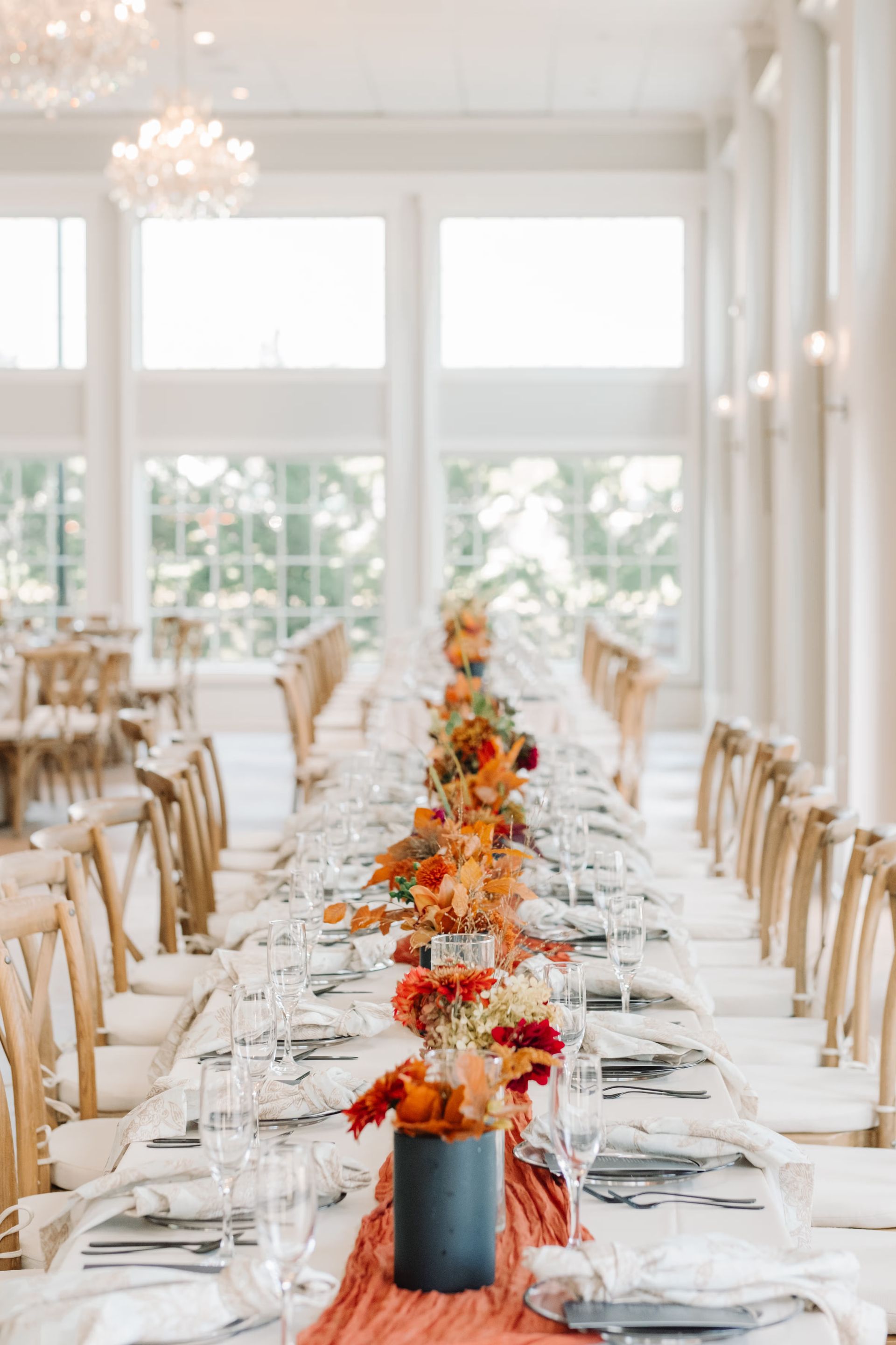 Elegant banquet table with orange floral centerpiece in a bright, airy event hall