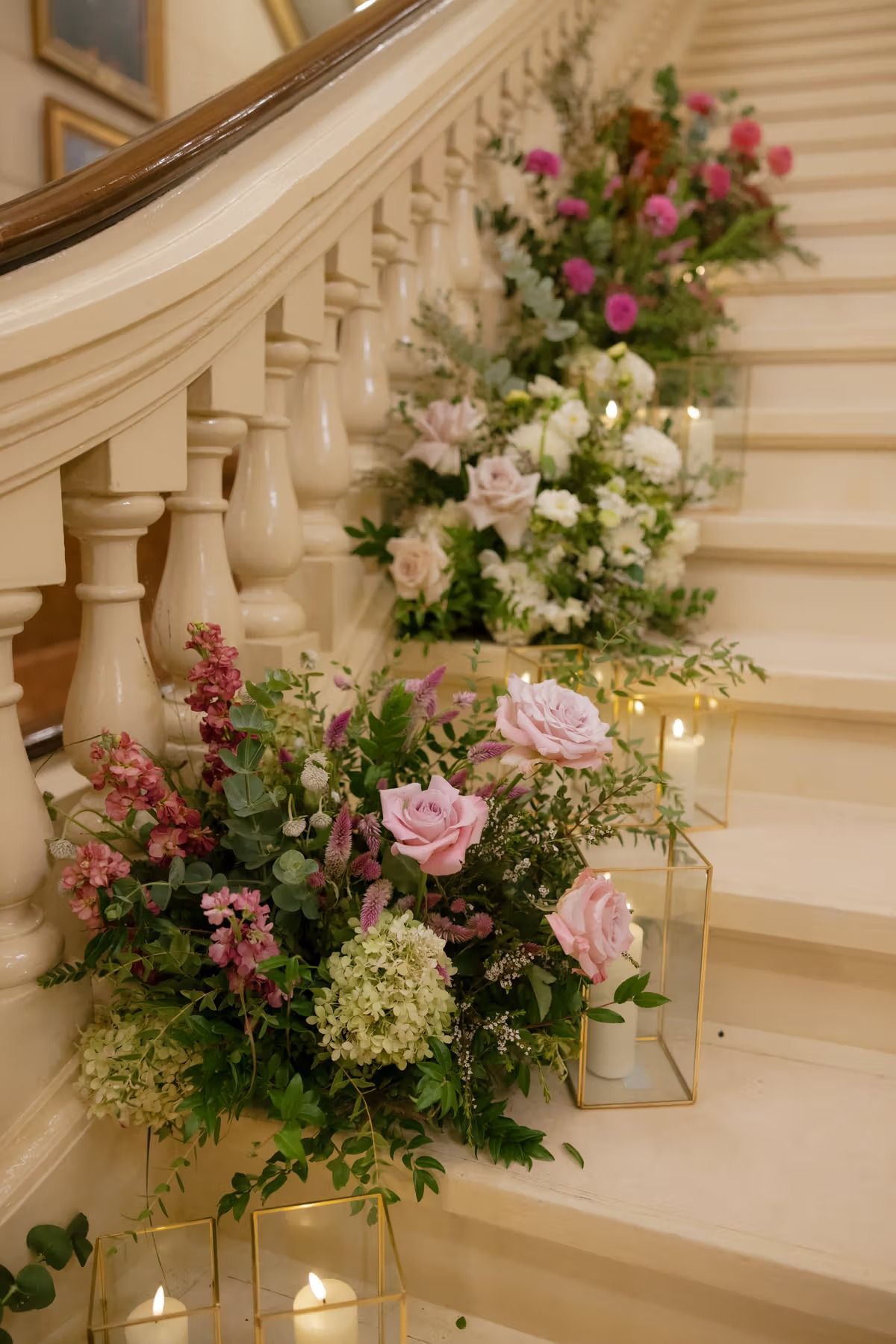 Flower arrangements lining a staircase with cream steps and white banister, decorated in pink, white, and green.