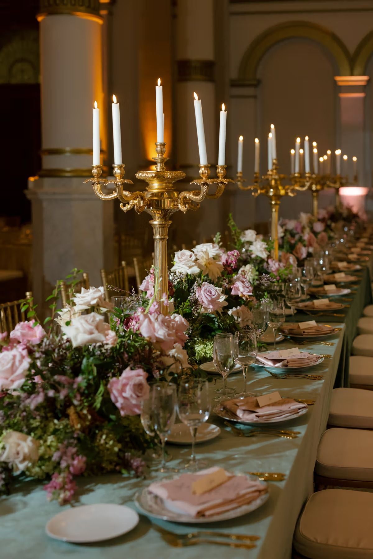Elegant banquet table set with gold candelabras and pink floral centerpieces in a grand hall