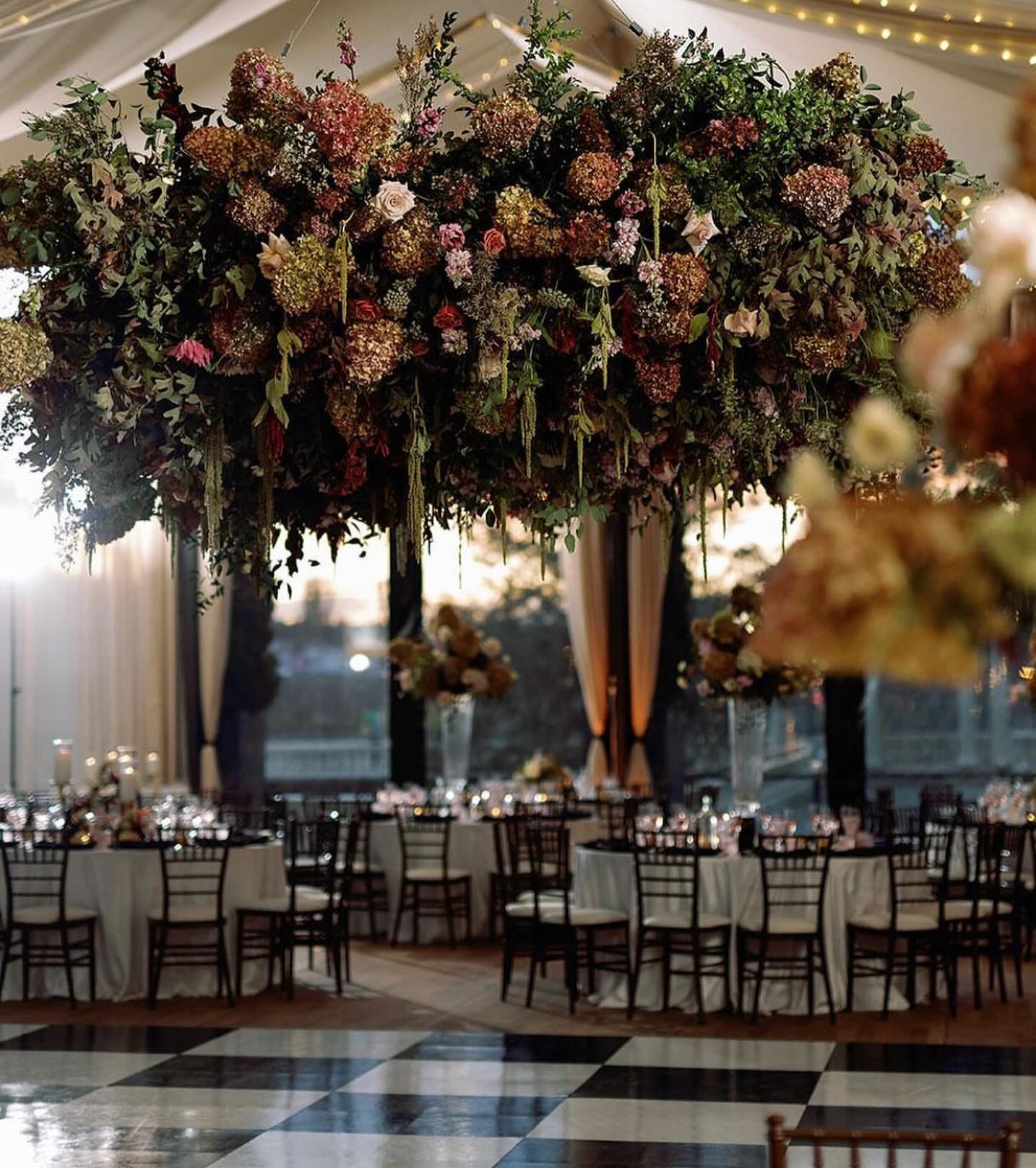 Elegant banquet hall with a large floral ceiling installation above set dining tables and chairs
