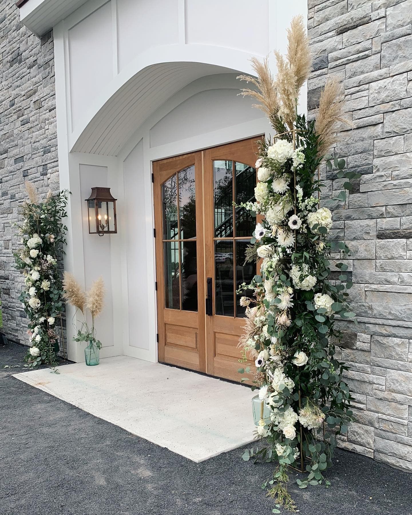 White arched entry with wooden double doors and floral arrangements on both sides