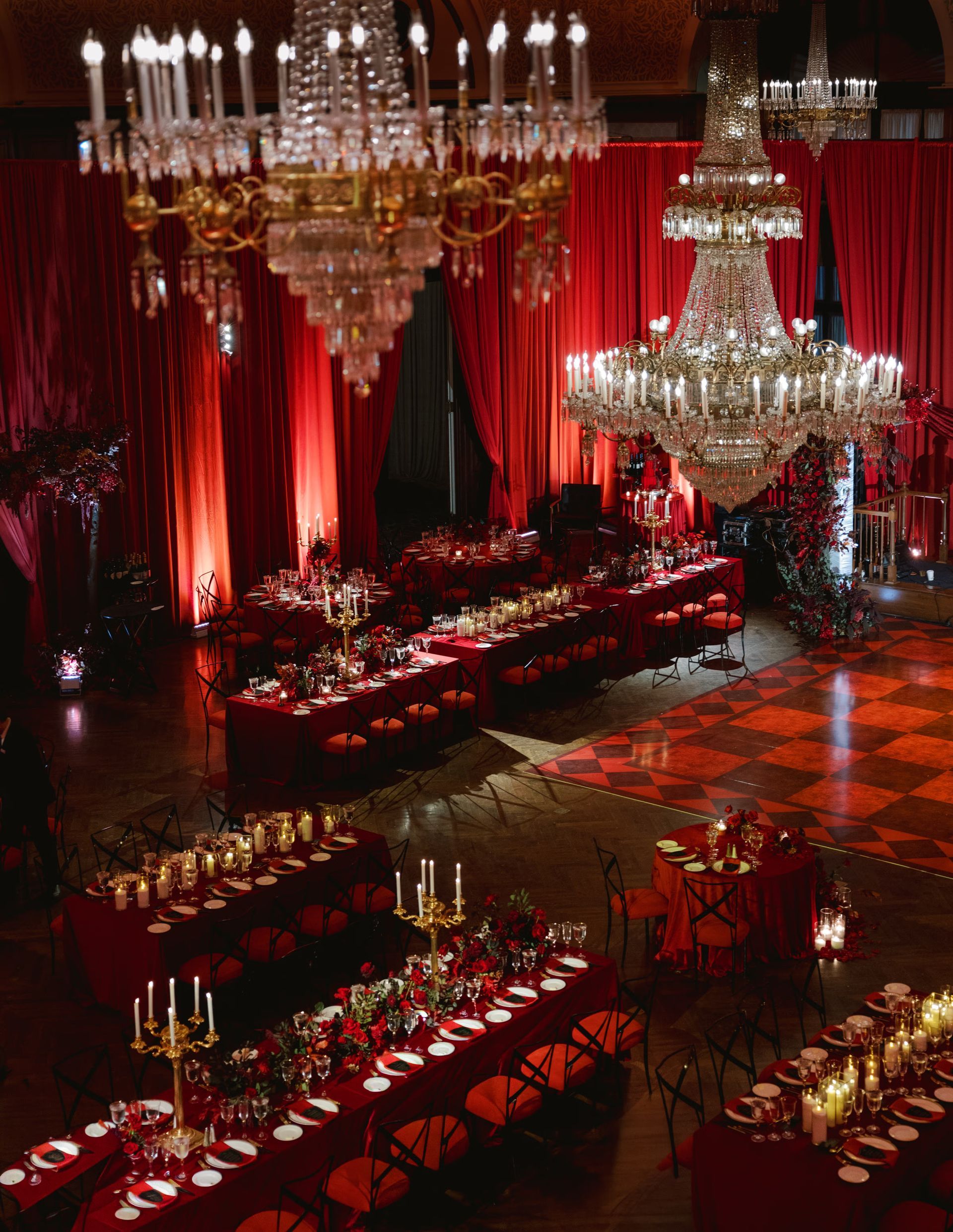 Red-lit banquet hall with chandeliers, long decorated tables, and a glossy patterned floor