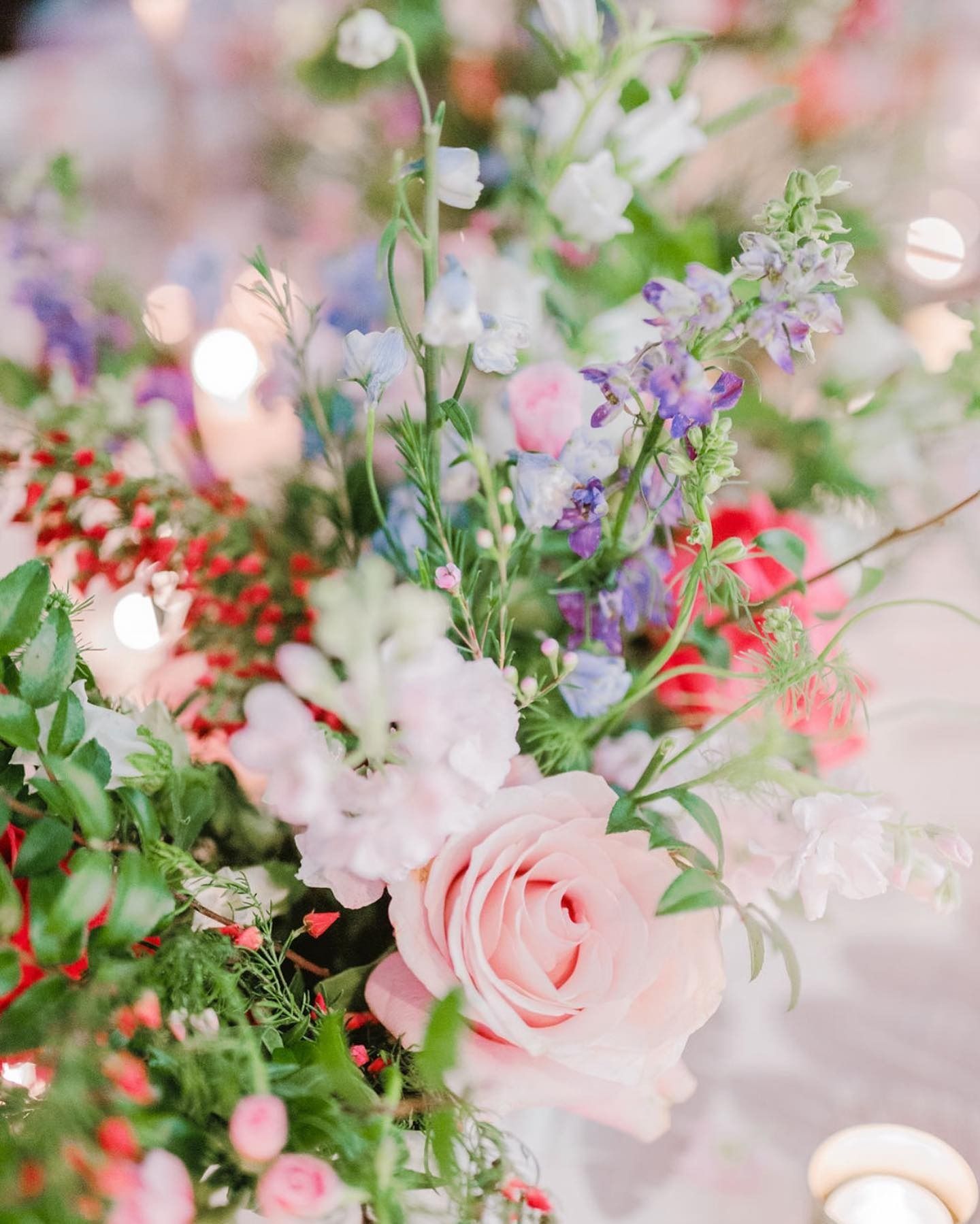 Pink roses and pastel wildflowers arranged in a soft, romantic floral bouquet with candlelight