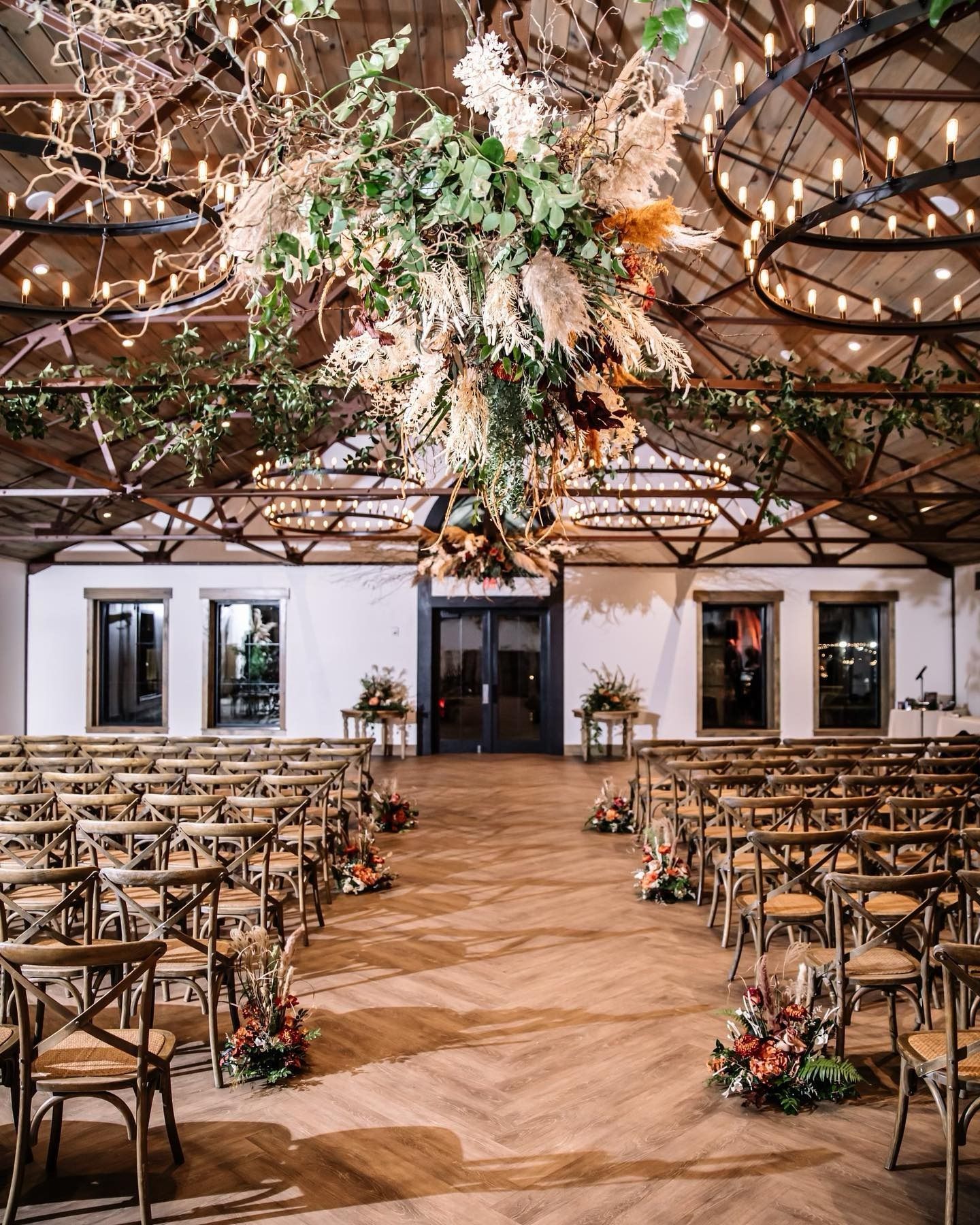 Elegant wedding venue with floral ceiling installation, rows of wooden chairs, and a central aisle