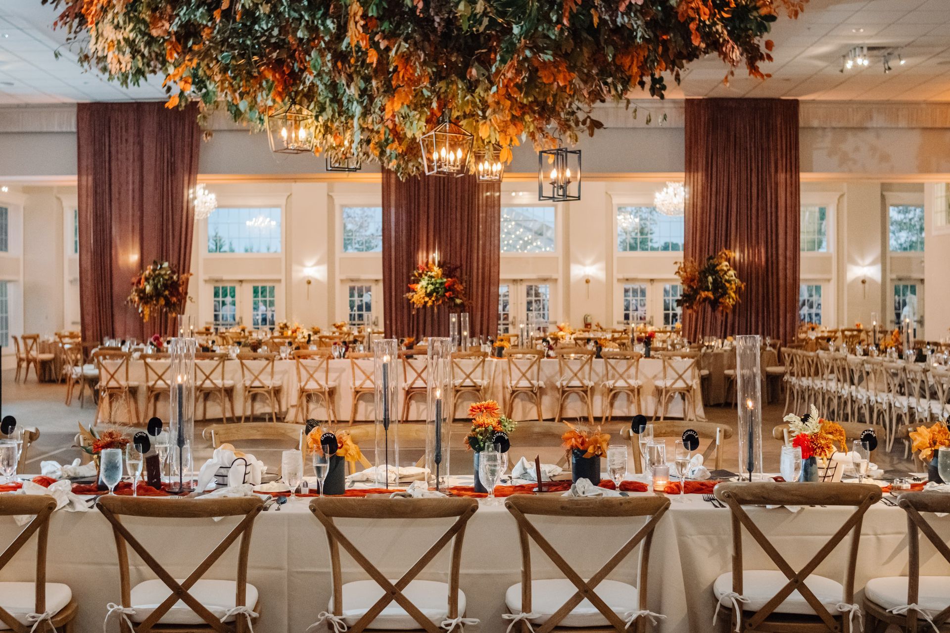 Elegant banquet hall with long tables, gold chairs, and warm floral ceiling decor