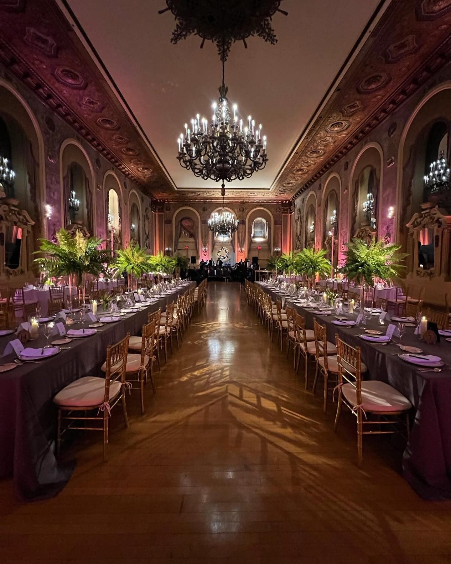 Elegant banquet hall with long candlelit tables, purple floral decor, and a chandelier overhead
