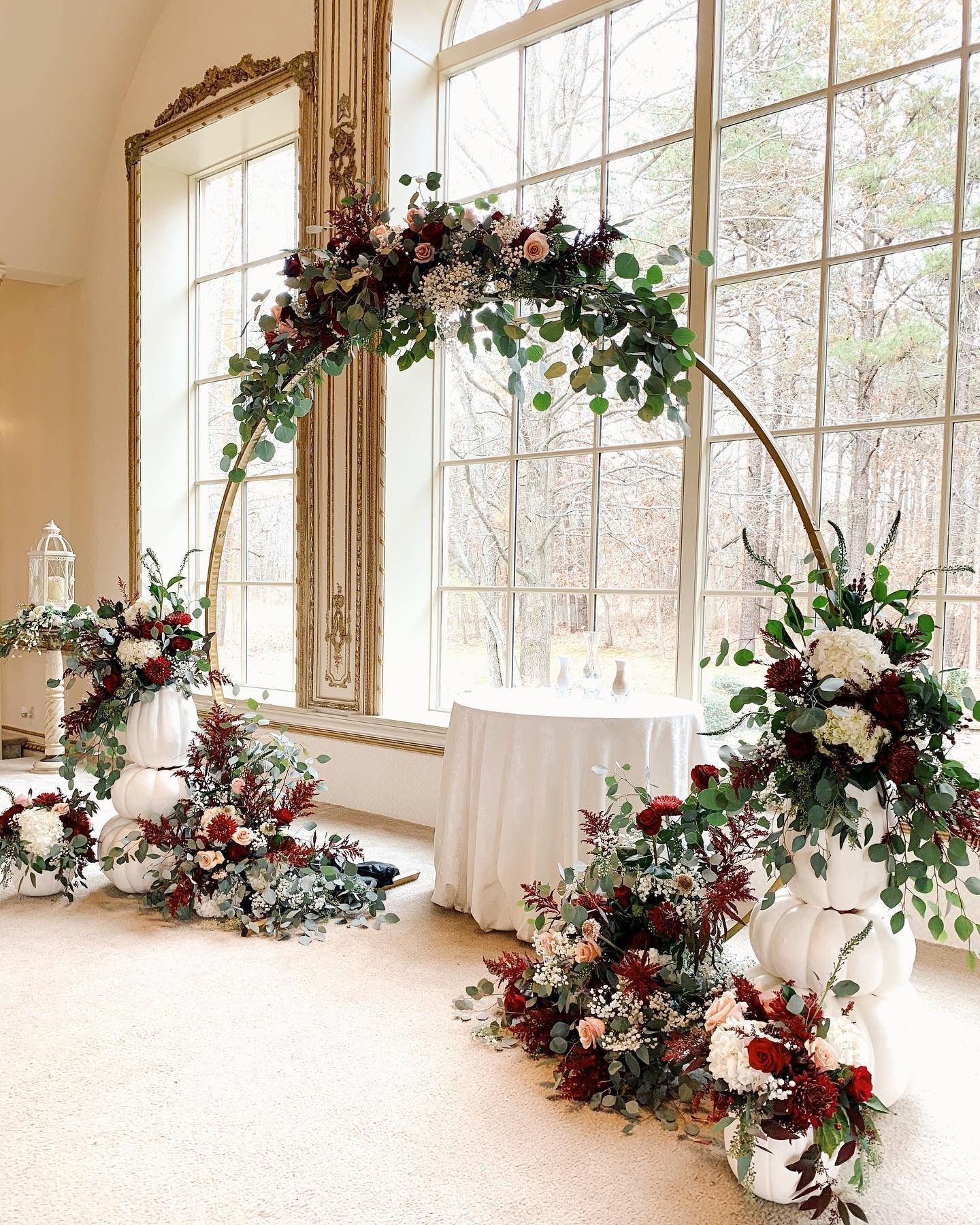 Elegant floral wedding arch and arrangements by a tall window in a bright room