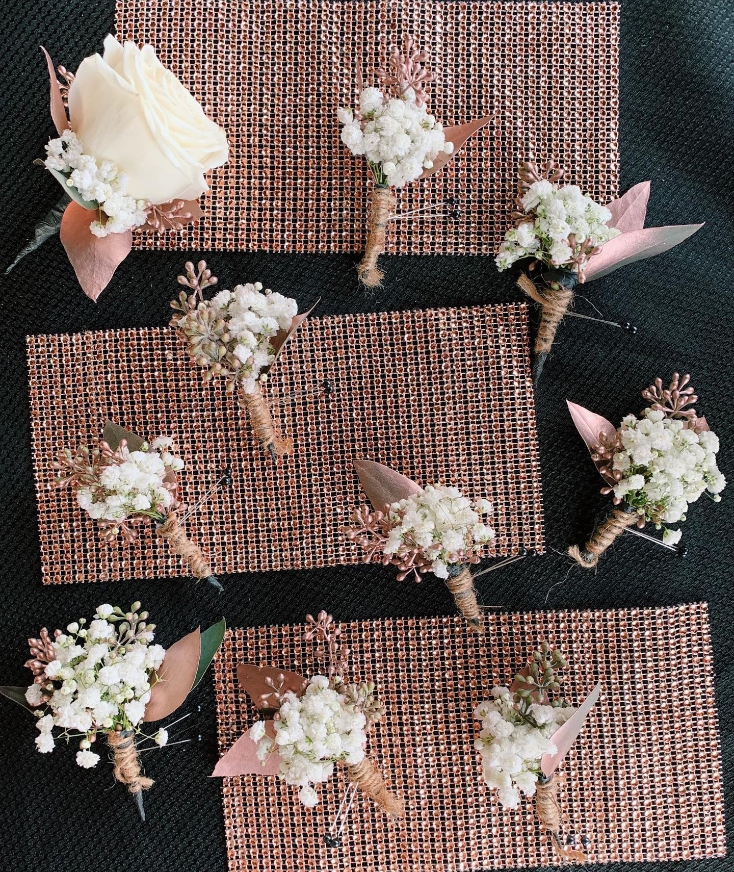 Small white flower bouquets with pink ribbons arranged on textured rose-gold placemats.