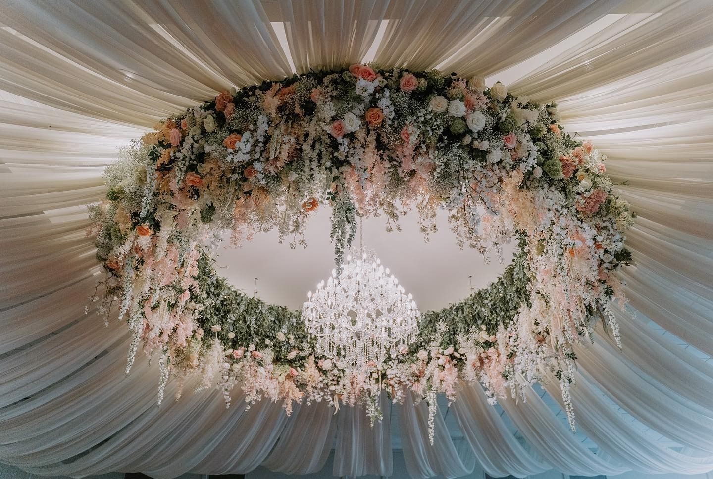 Floral ring ceiling centerpiece with pink, white, and green flowers around a hanging crystal chandelier