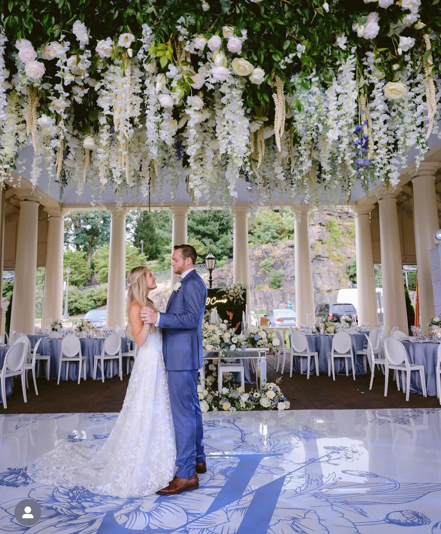 Bride and groom dancing beneath hanging white flowers in an elegant garden pavilion
