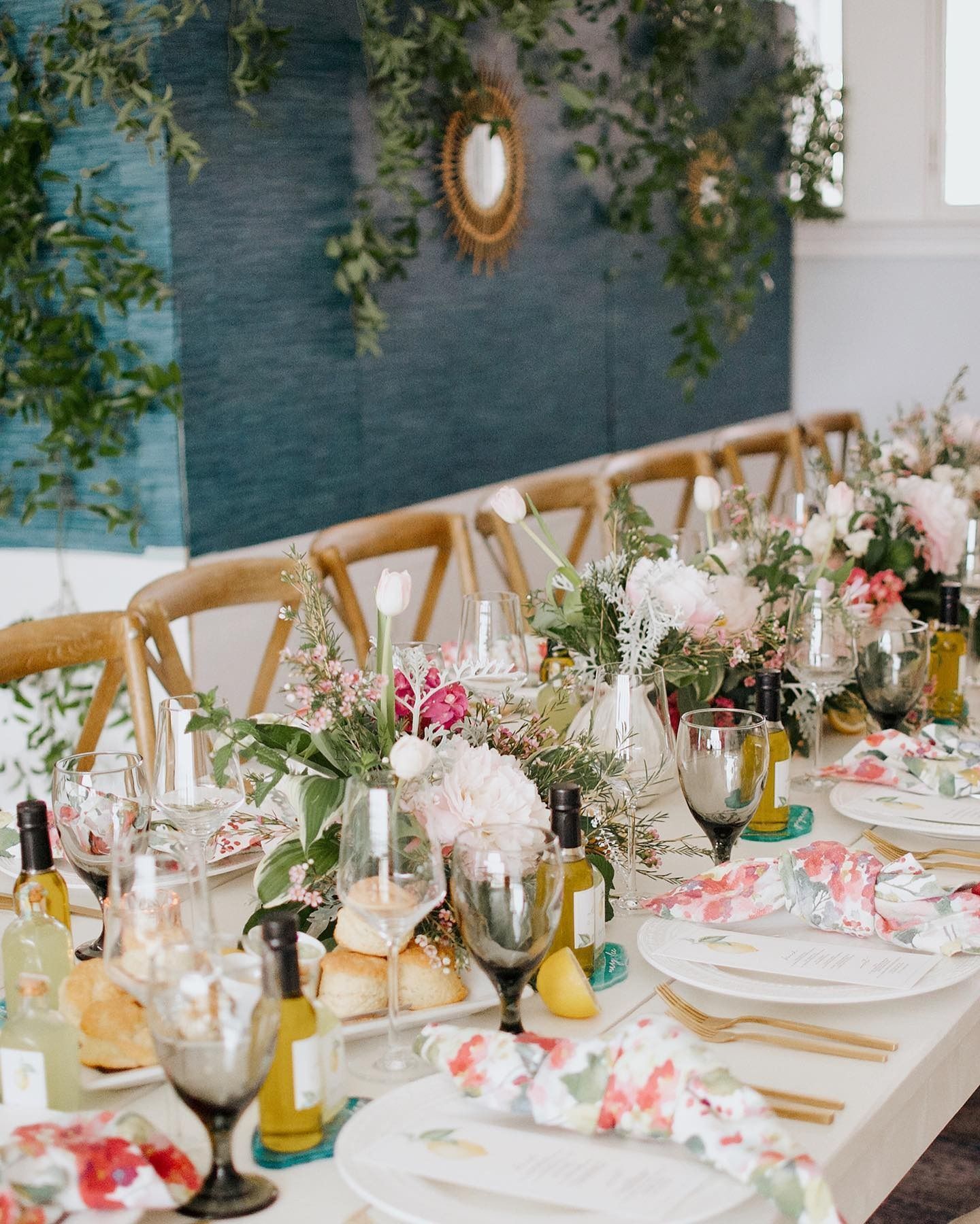 Elegant floral dining table set with white plates, glassware, and candles beside a blue wall and greenery
