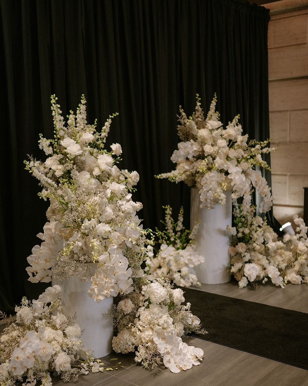 Tall white floral arrangements on pedestal vases in a dim indoor venue