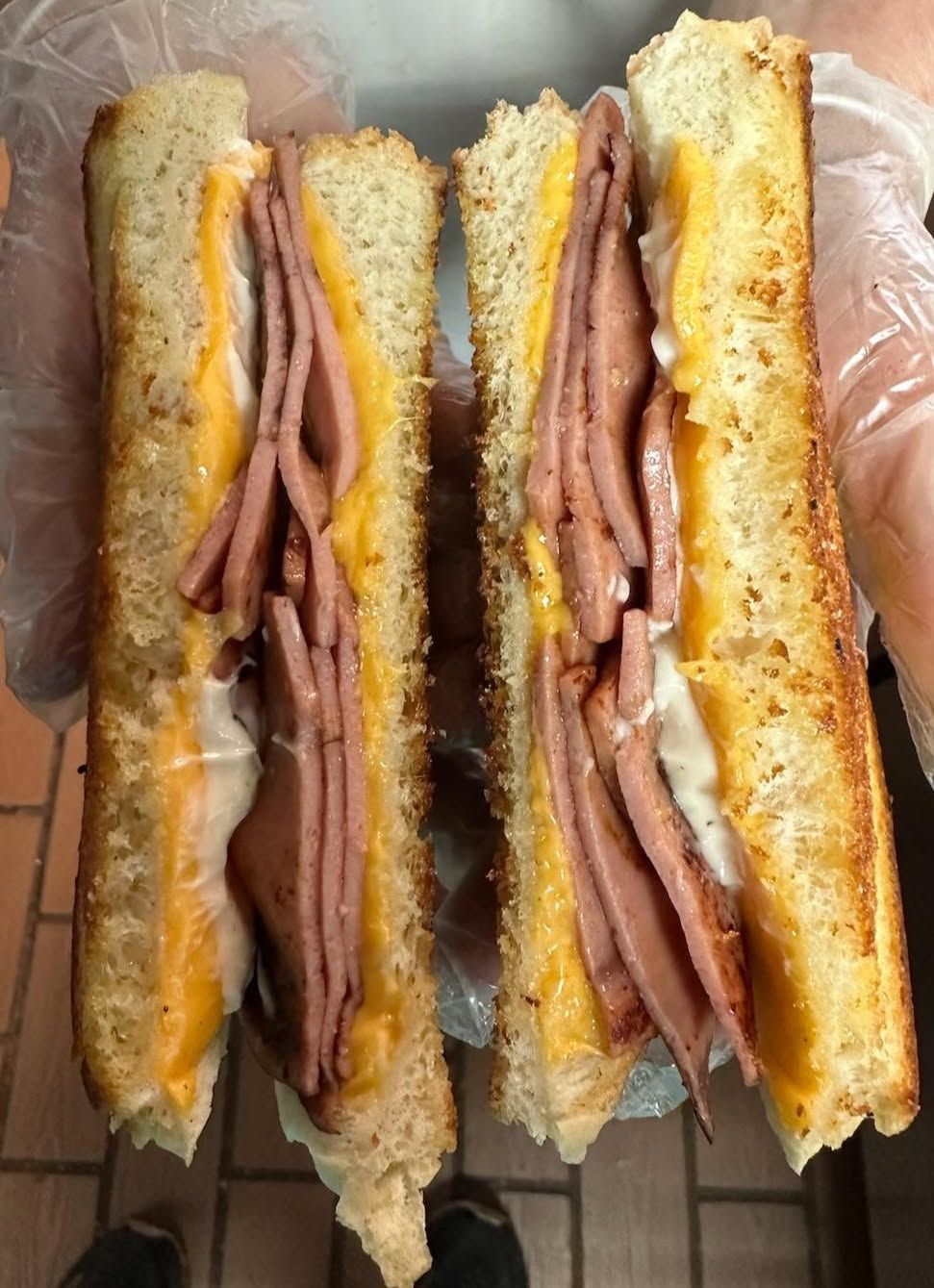 Close-up of a grilled sandwich cut in half, showing layers of ham and melted cheese in a gloved hand