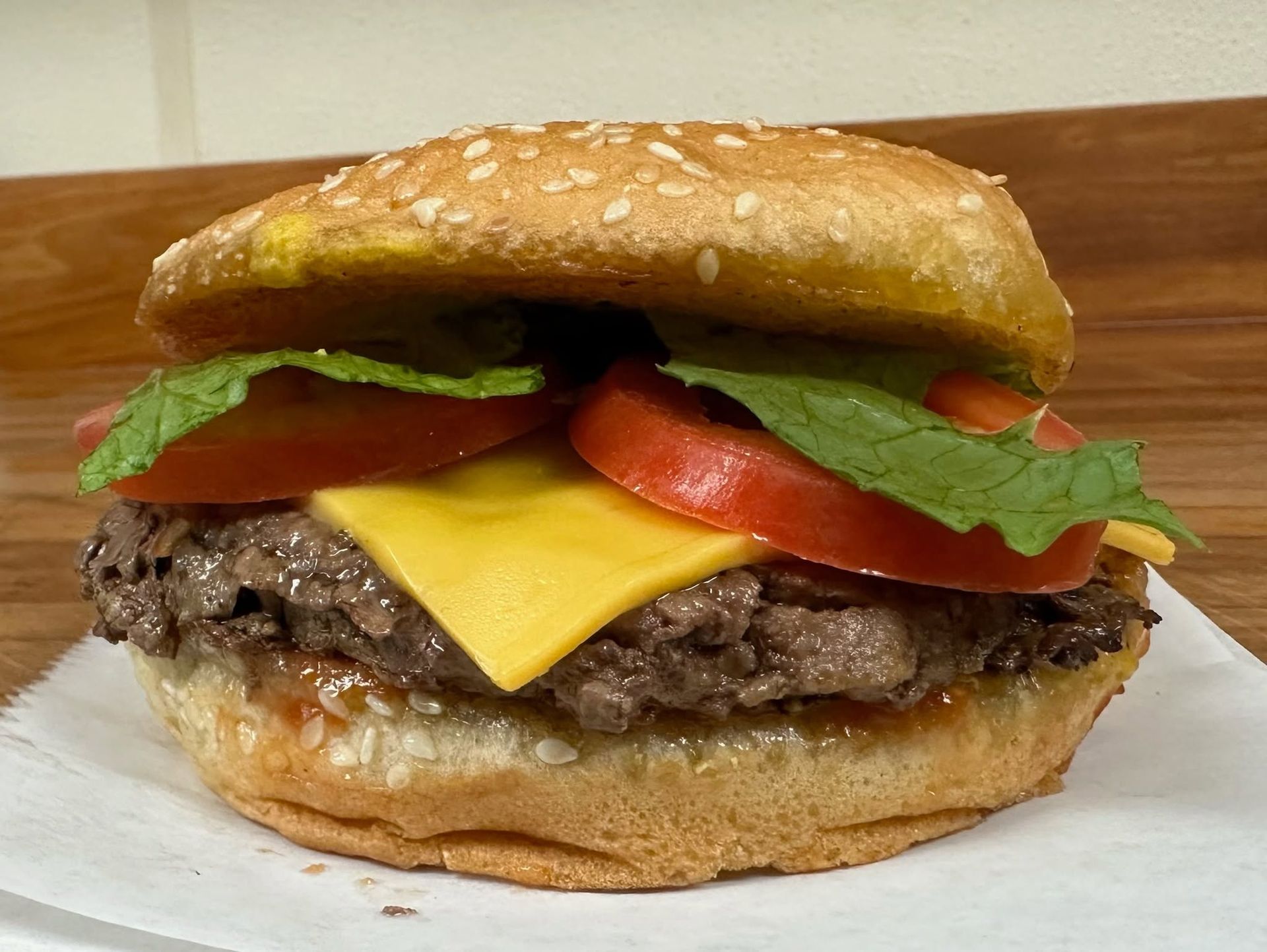 Close-up of a hamburger with cheese, tomato, and lettuce on a bun on a wooden surface
