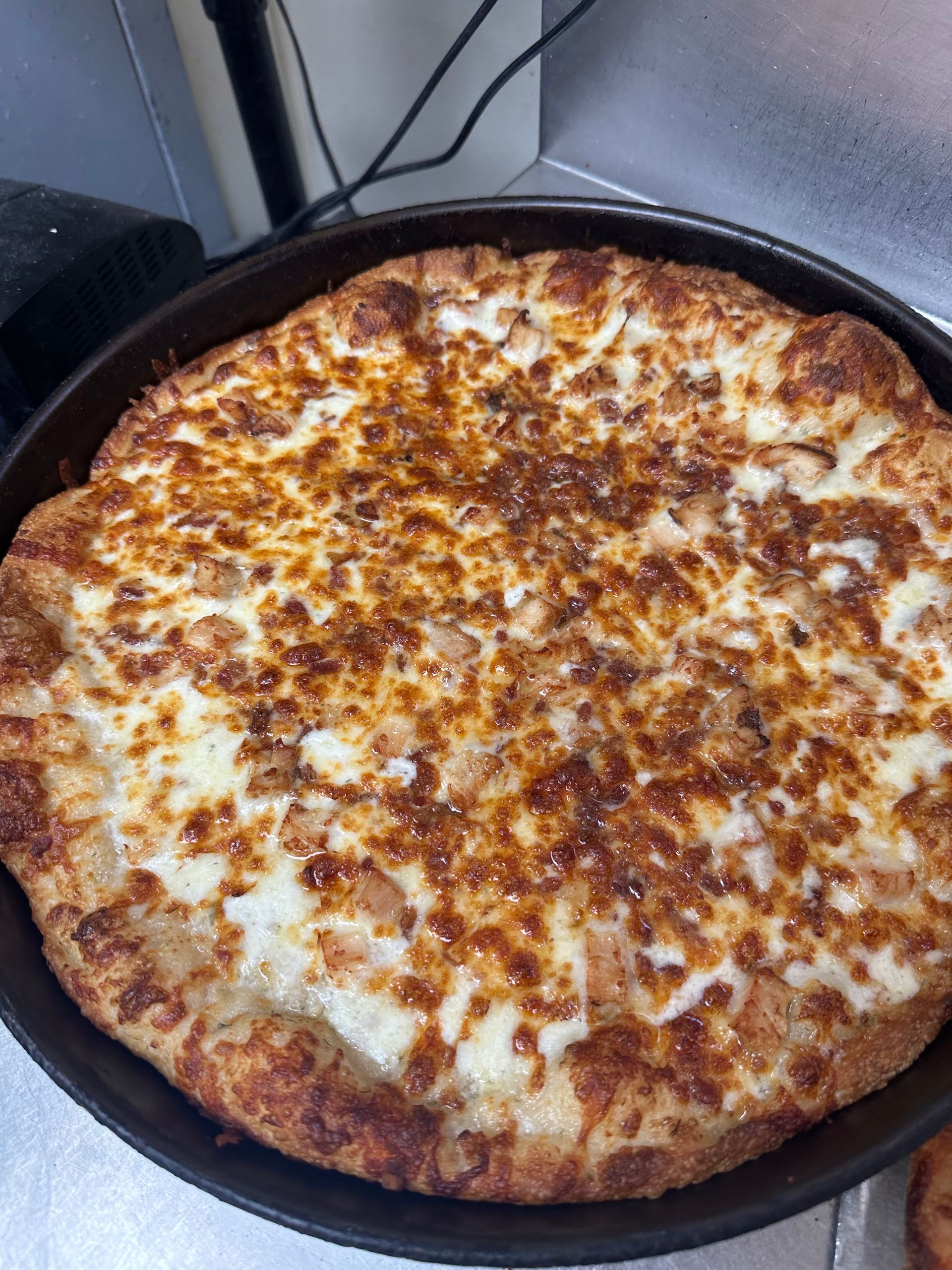 Cheesy baked pizza in a black skillet, golden brown on top with a thick crust
