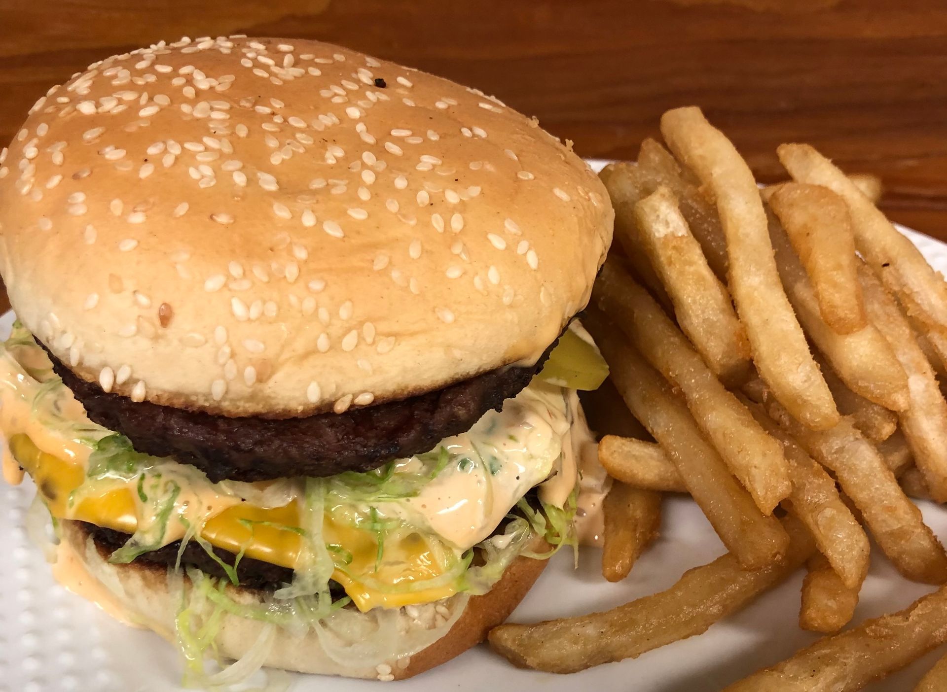 Sesame-seed burger with lettuce and cheese beside French fries on a plate