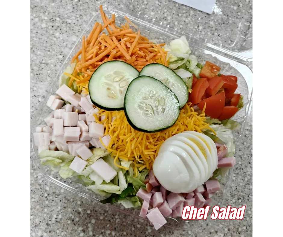 Tray of layered chopped salad with avocado, hard-boiled eggs, tomatoes, corn, shredded carrots, meat, and herbs