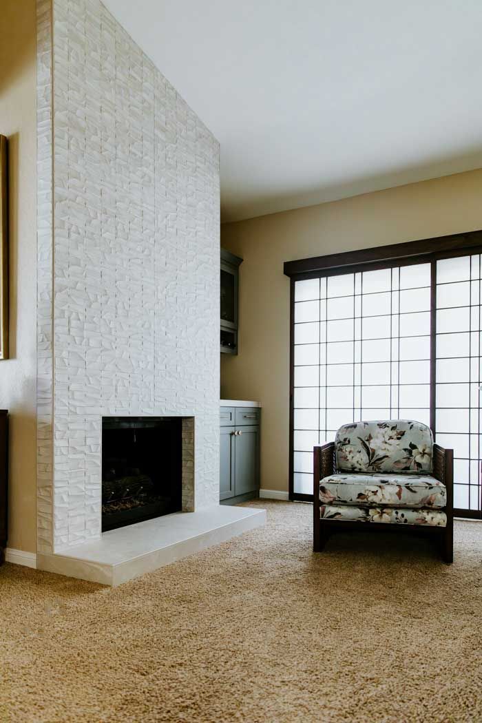 A living room with a fireplace , chair and sliding glass doors.