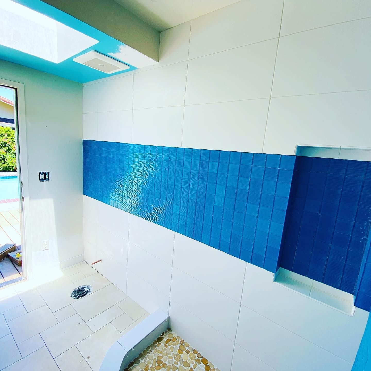 A bathroom with blue and white tiles and a door leading to a pool.