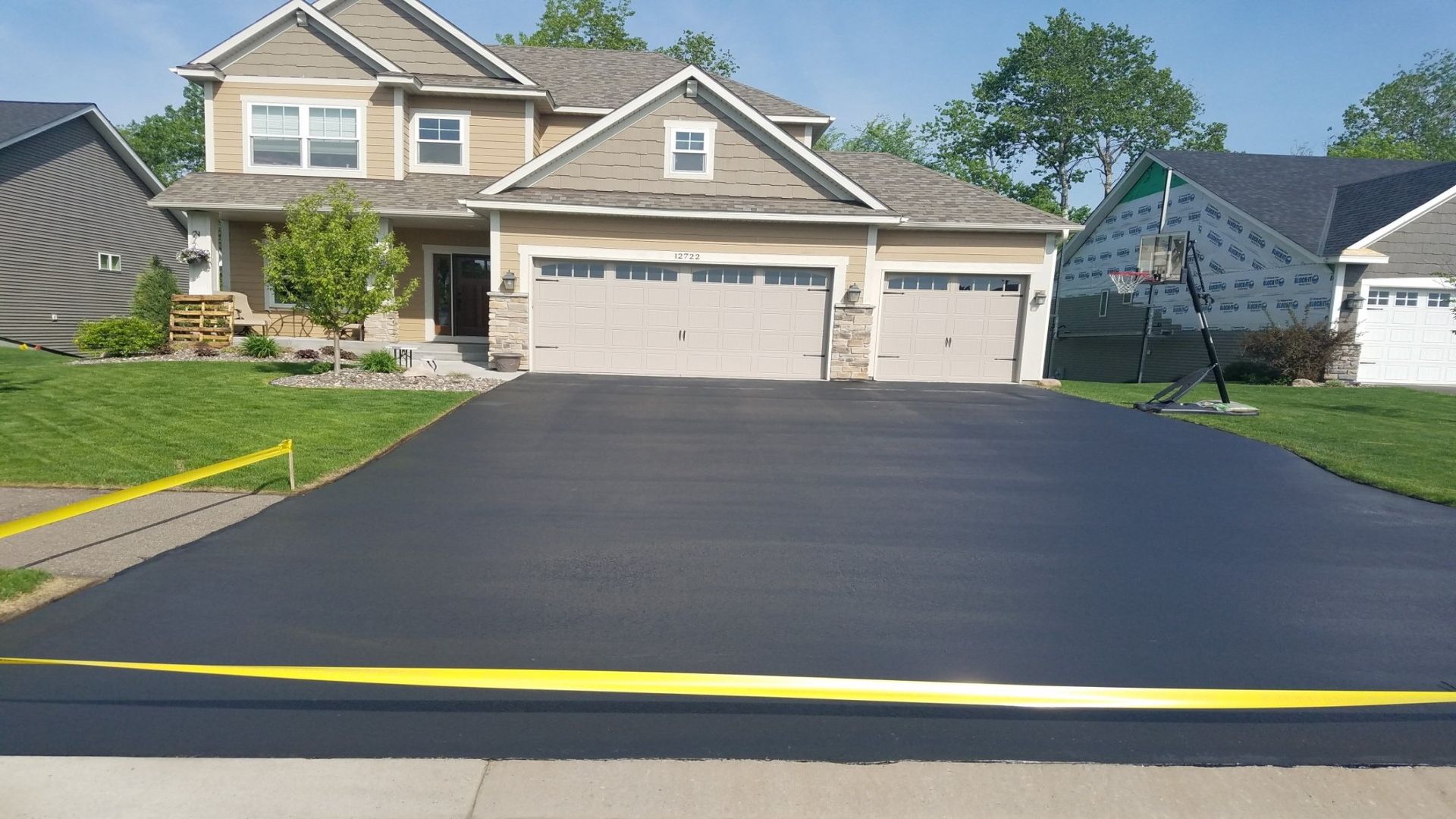 Freshly paved black asphalt driveway leading to a beige suburban house with two garage doors