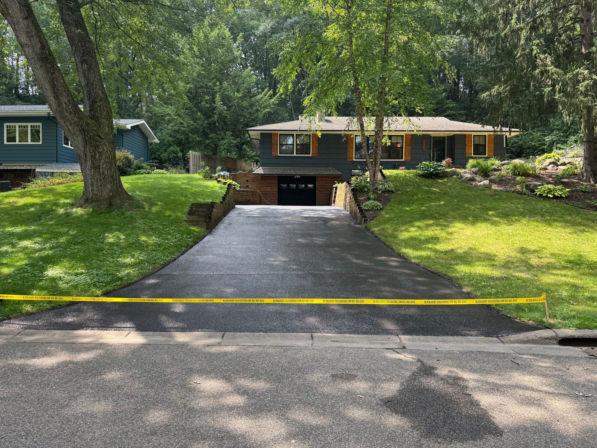 Driveway leading to a brick house in a wooded suburban yard with green grass and trees