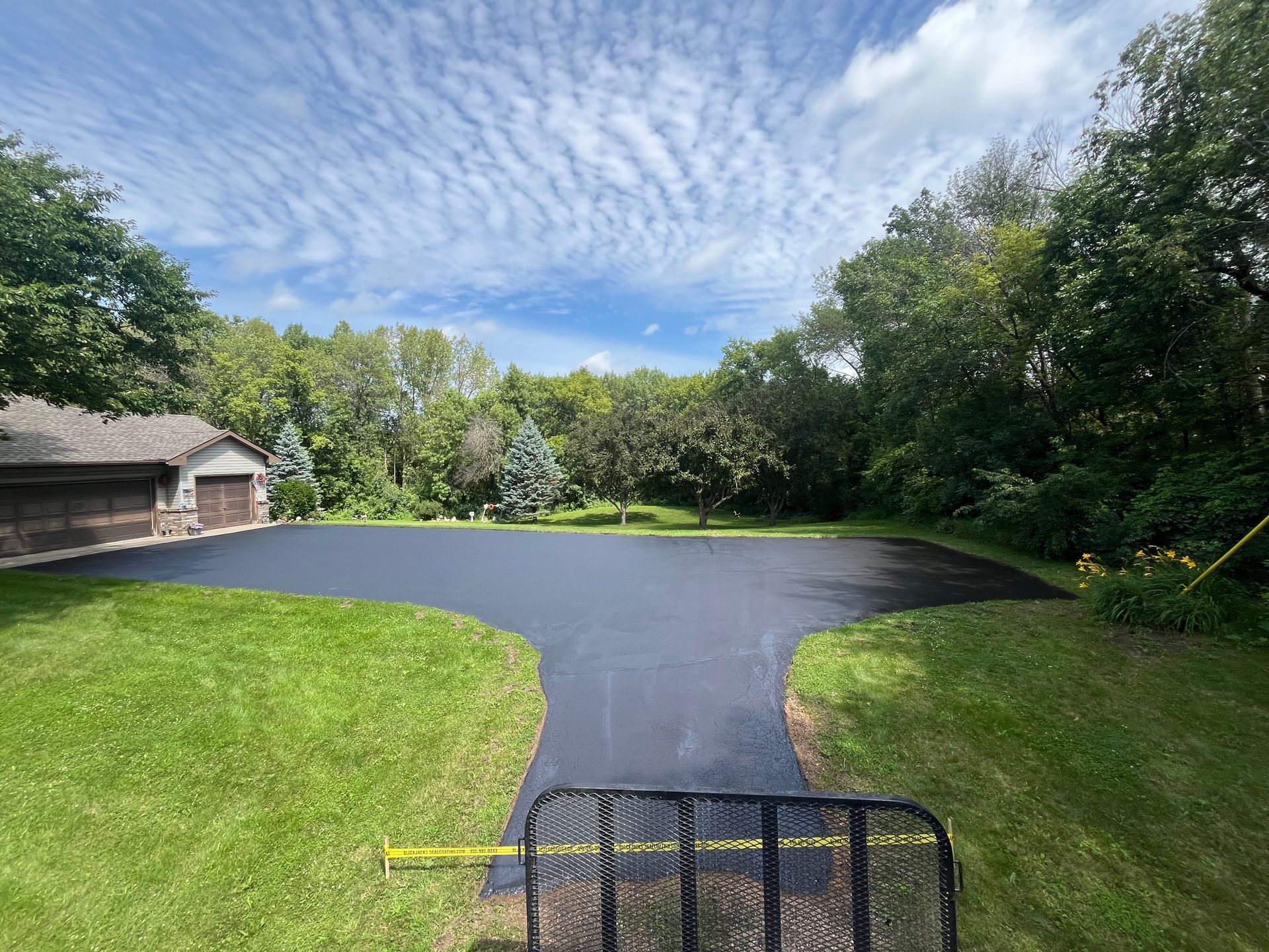 Curved blacktop driveway beside green lawn and trees under a partly cloudy sky