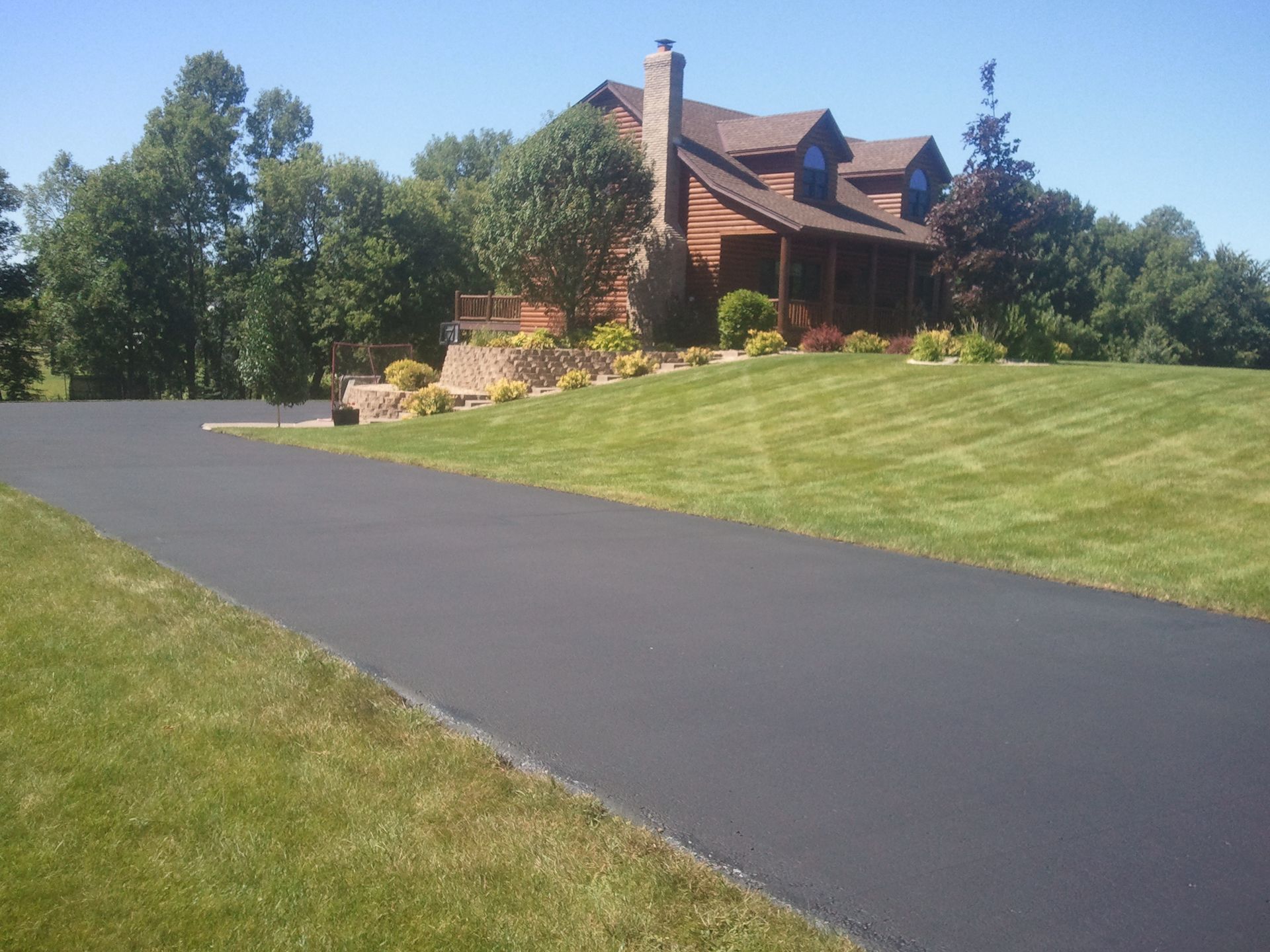 Large brick house with a winding driveway and landscaped lawn on a sunny day
