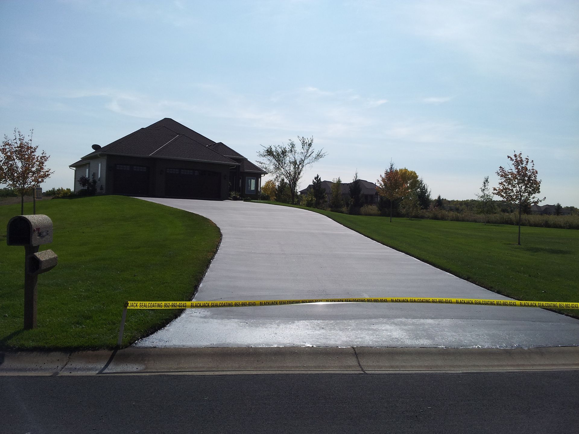 Suburban driveway blocked by yellow caution tape leading to a house on a grassy hill