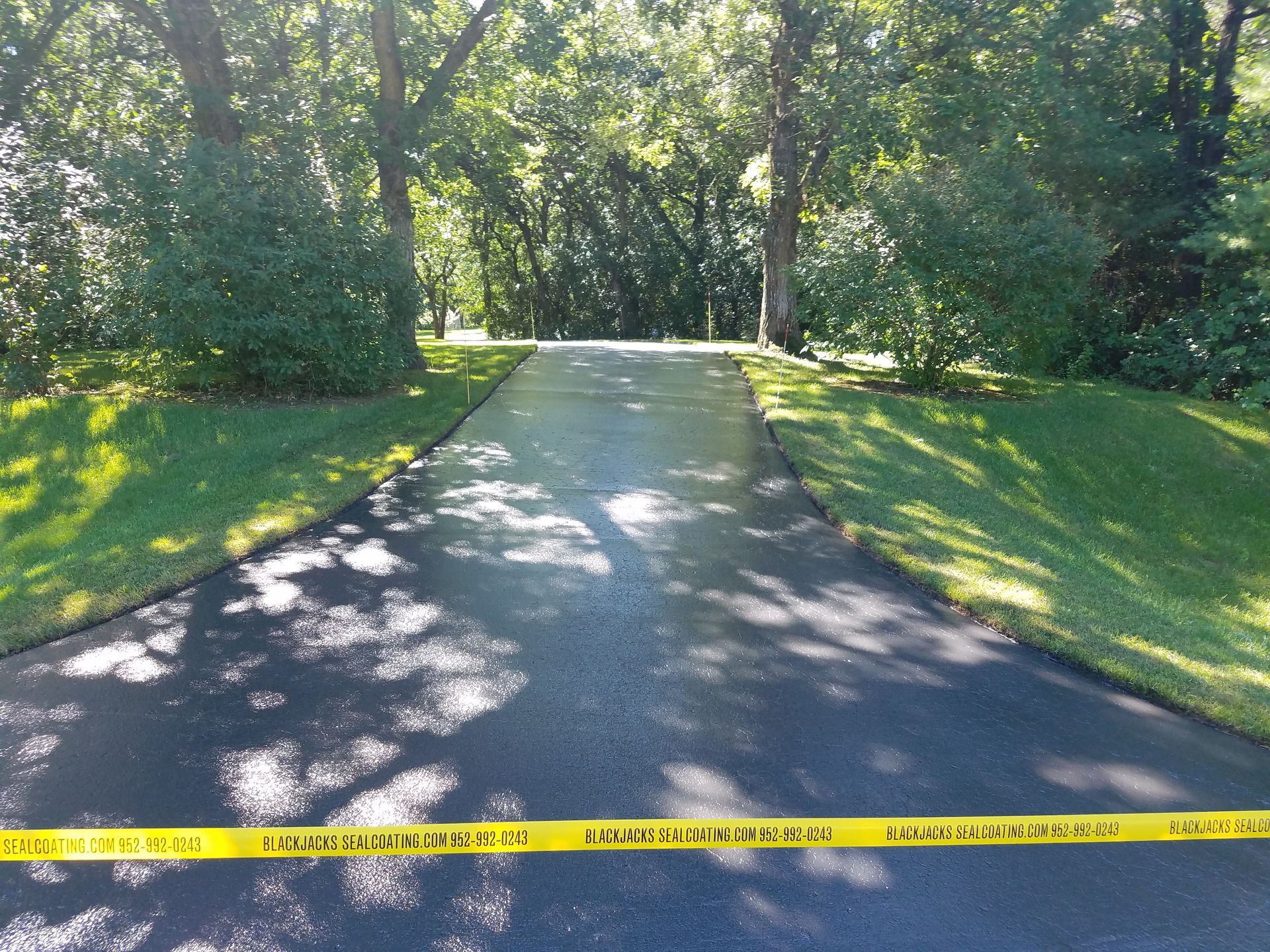 Sunlit driveway leading through trees, blocked by yellow caution tape across the foreground.